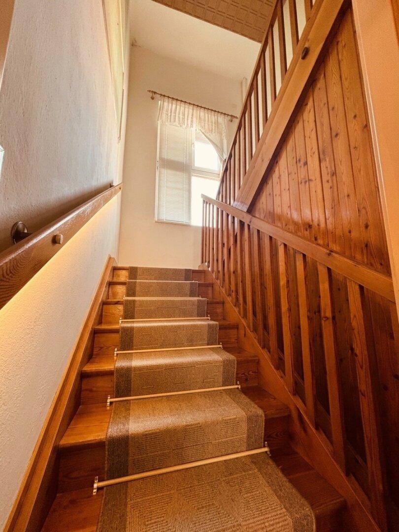 Holztreppe mit Teppichläufer und Fenster im Treppenhaus.