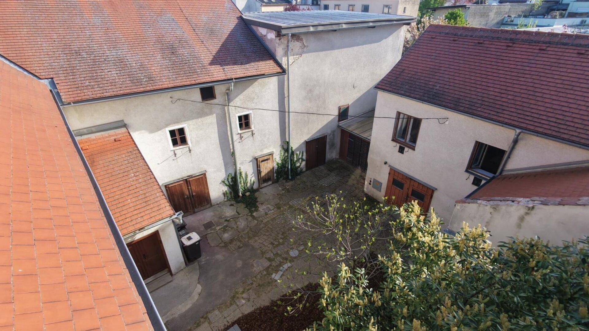 Blick von oben auf den gepflasterten Innenhof, umgeben von Gebäuden mit roten Ziegeldächern.