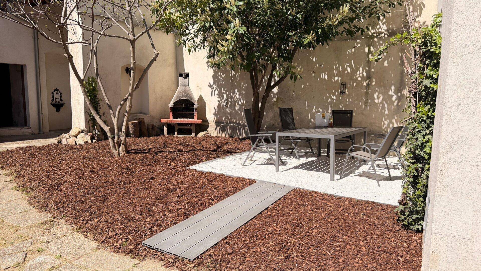Gemütlicher Gartenbereich mit Sitzgelegenheiten, Grill und Bäumen, ideal zum Entspannen.