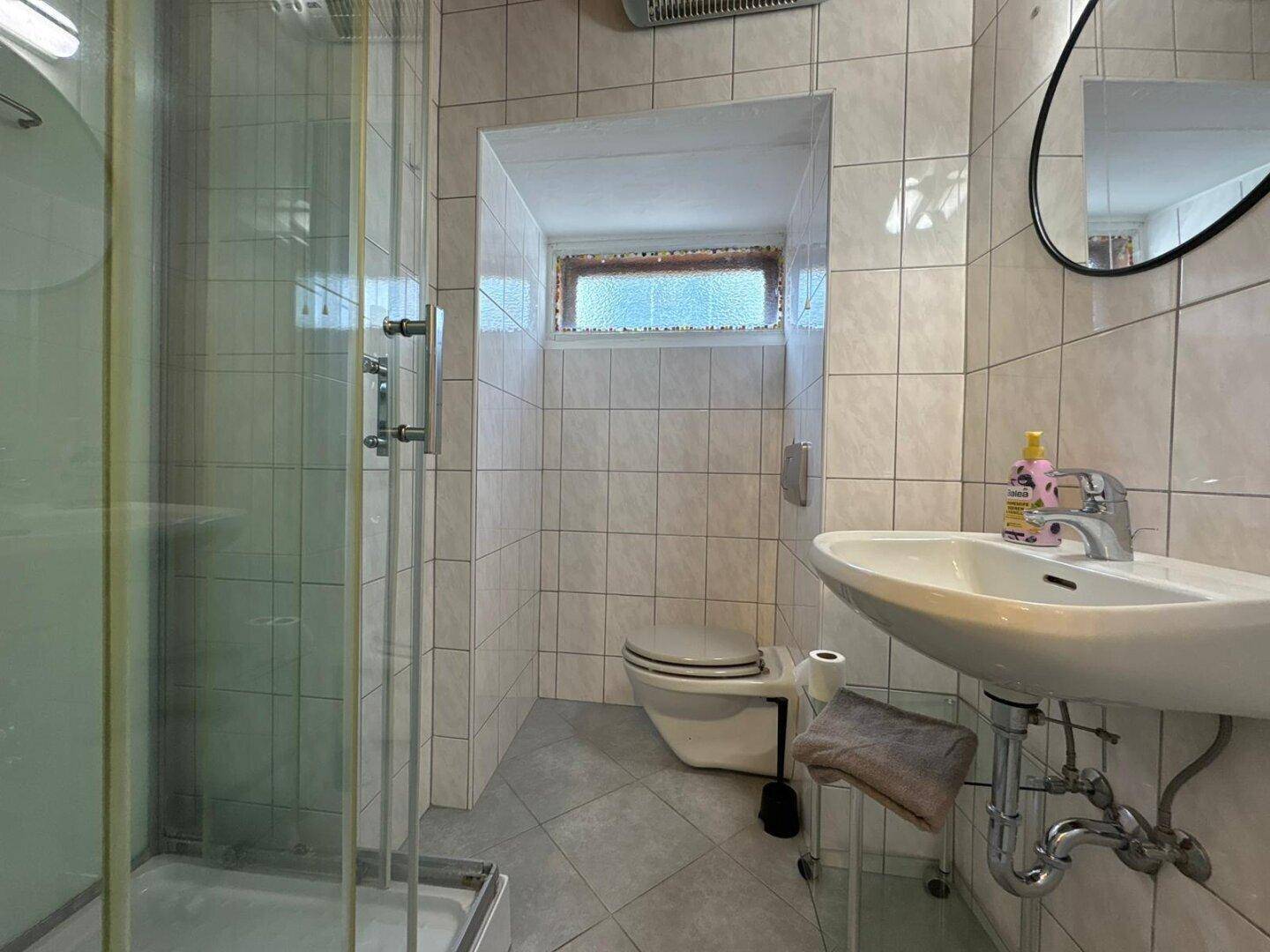 Modernes Badezimmer mit Duschkabine, WC und Waschbecken, komplett gefliest.