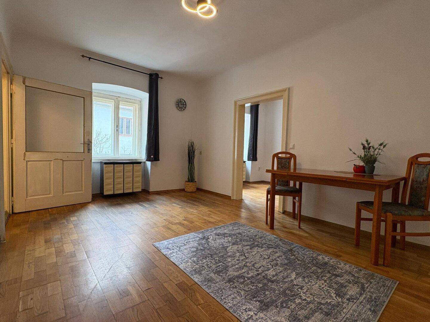 Helles Wohnzimmer mit Parkettboden, dekorativem Teppich und großen Fenstern.