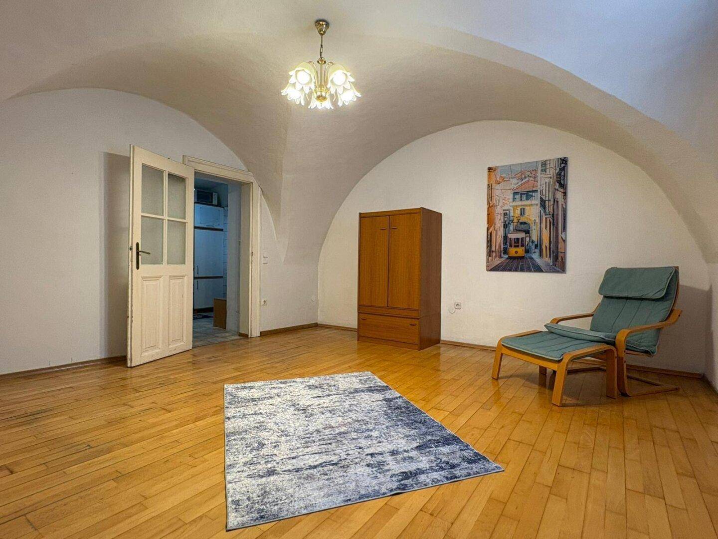 Geräumiges Wohnzimmer mit Holzboden, gewölbter Decke und einem dekorativen Teppich.