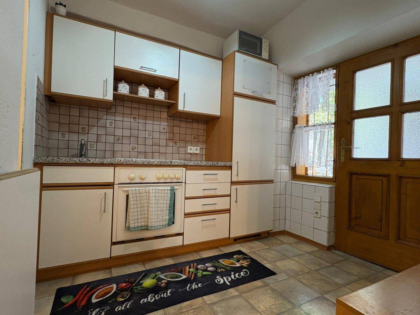 Traditionelle Küche mit weißen Schränken, Fliesenrückwand und Fenster mit Vorhängen.
