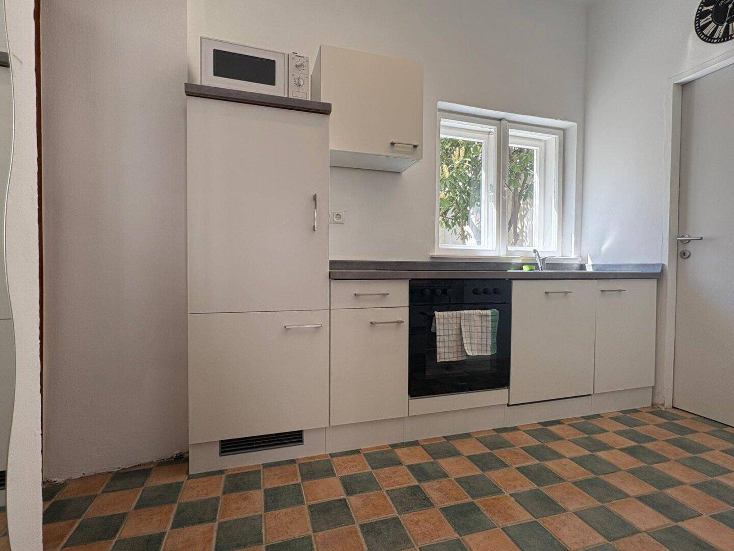 Helle Küche mit modernen weißen Schränken, Mikrowelle und kariertem Fliesenboden.