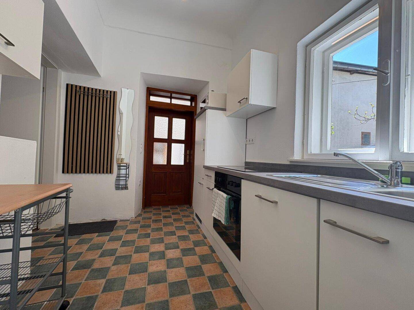Funktionale Küche mit kariertem Fliesenboden, Einbaugeräten und Fenster mit Blick nach draußen.
