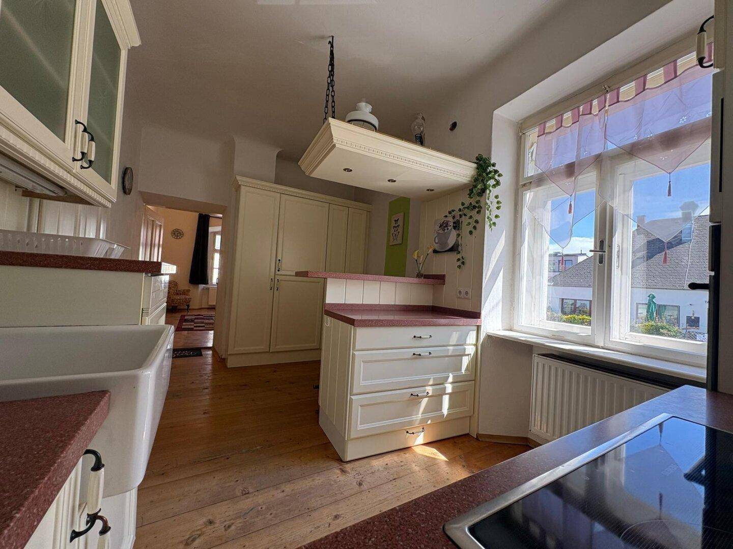 Helle Landhausküche mit roten Arbeitsplatten, Spülbecken und Fenster mit Blick ins Grüne.