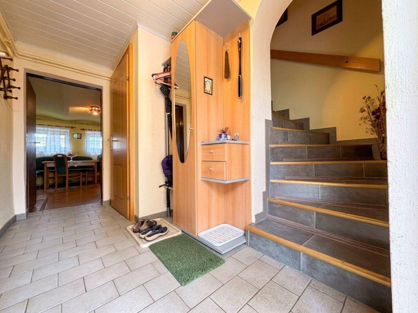 Heller Eingangsbereich mit Fliesenboden, Holzgarderobe und Treppe zum Obergeschoss.
