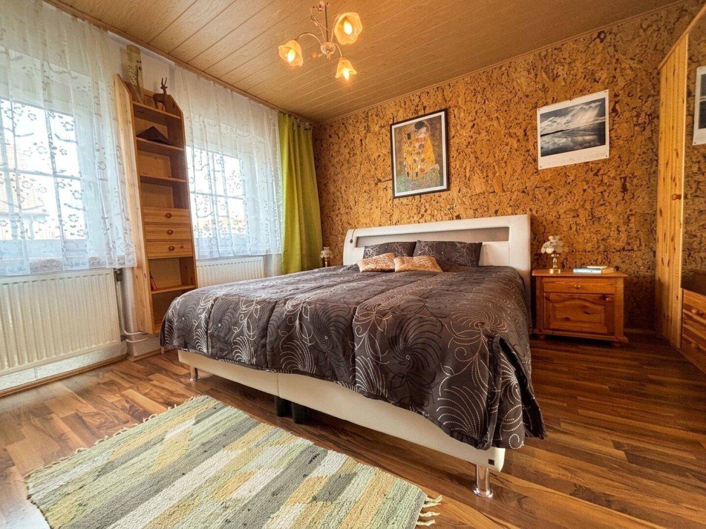 Schlafzimmer mit Holzboden, Doppelbett und Fenster, das viel Tageslicht hereinlässt.