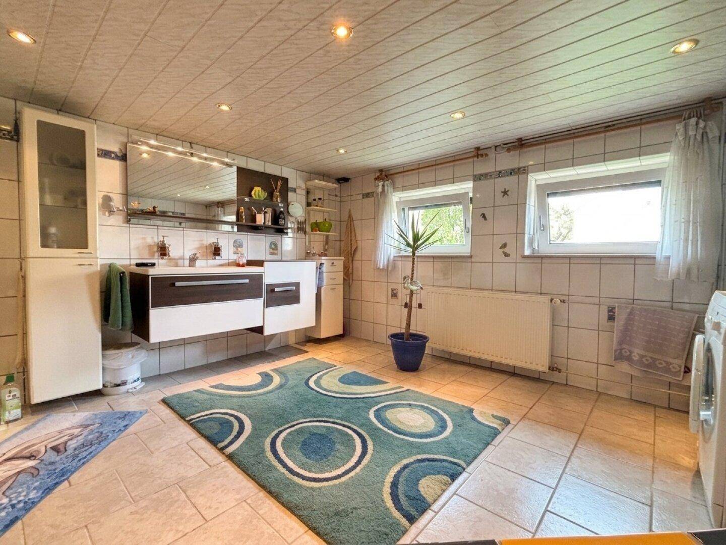 Geräumiges Badezimmer mit Fliesenboden, modernem Doppelwaschbecken und Waschmaschine.