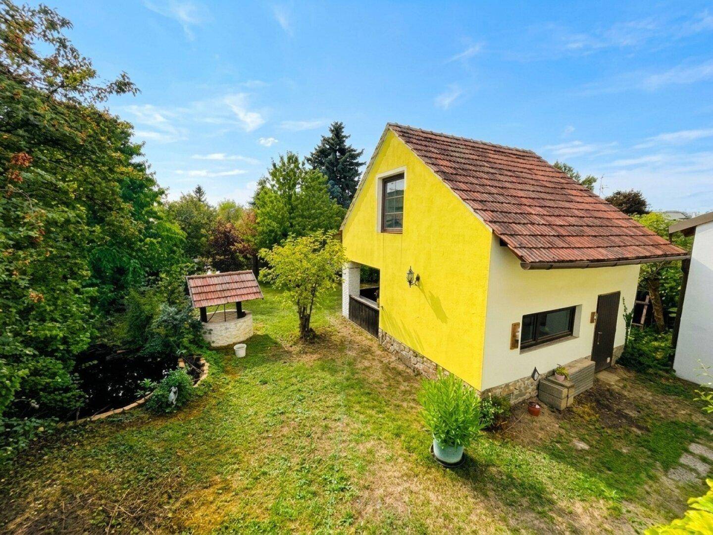 Übersicht des Hauses und des weitläufigen Gartens mit Brunnen unter blauem Himmel.