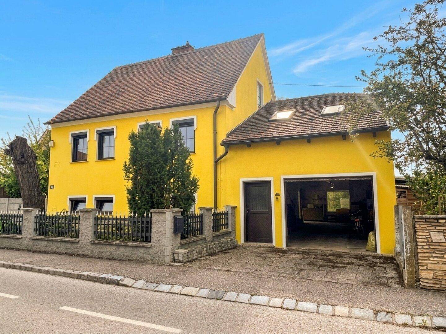 Vorderansicht des gelben Hauses mit integrierter Garage und gepflegtem Vorgarten.