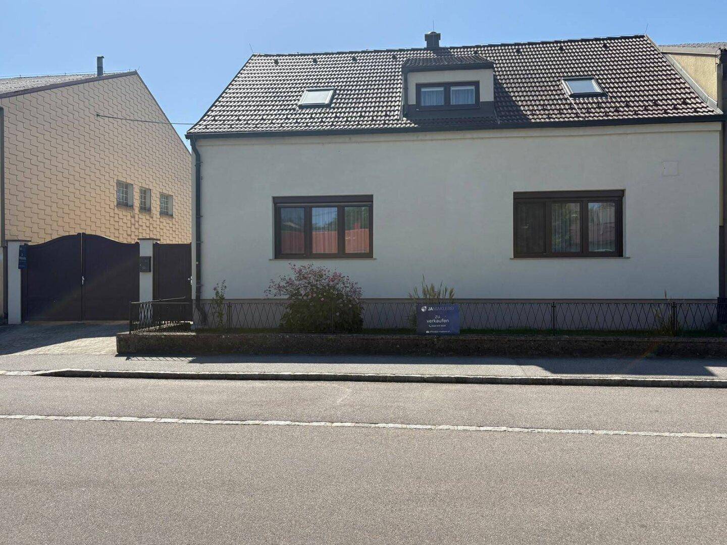 Ansicht des Hauses von der Straße aus mit beiger Fassade, Satteldach und einem kleinen Vorgarten.