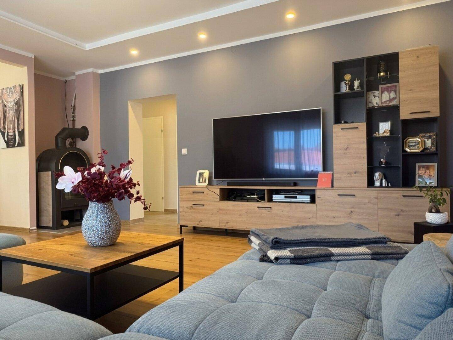 Wohnzimmer mit Kaminofen, großem Fernseher und moderner Wohnwand.