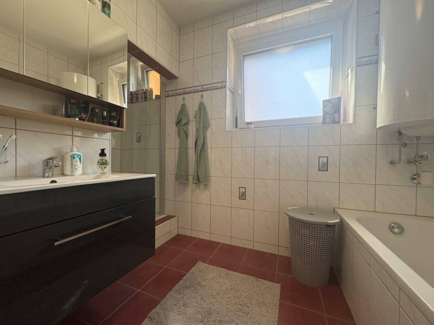 Badezimmer mit Badewanne, Dusche, Waschbecken und Fenster.