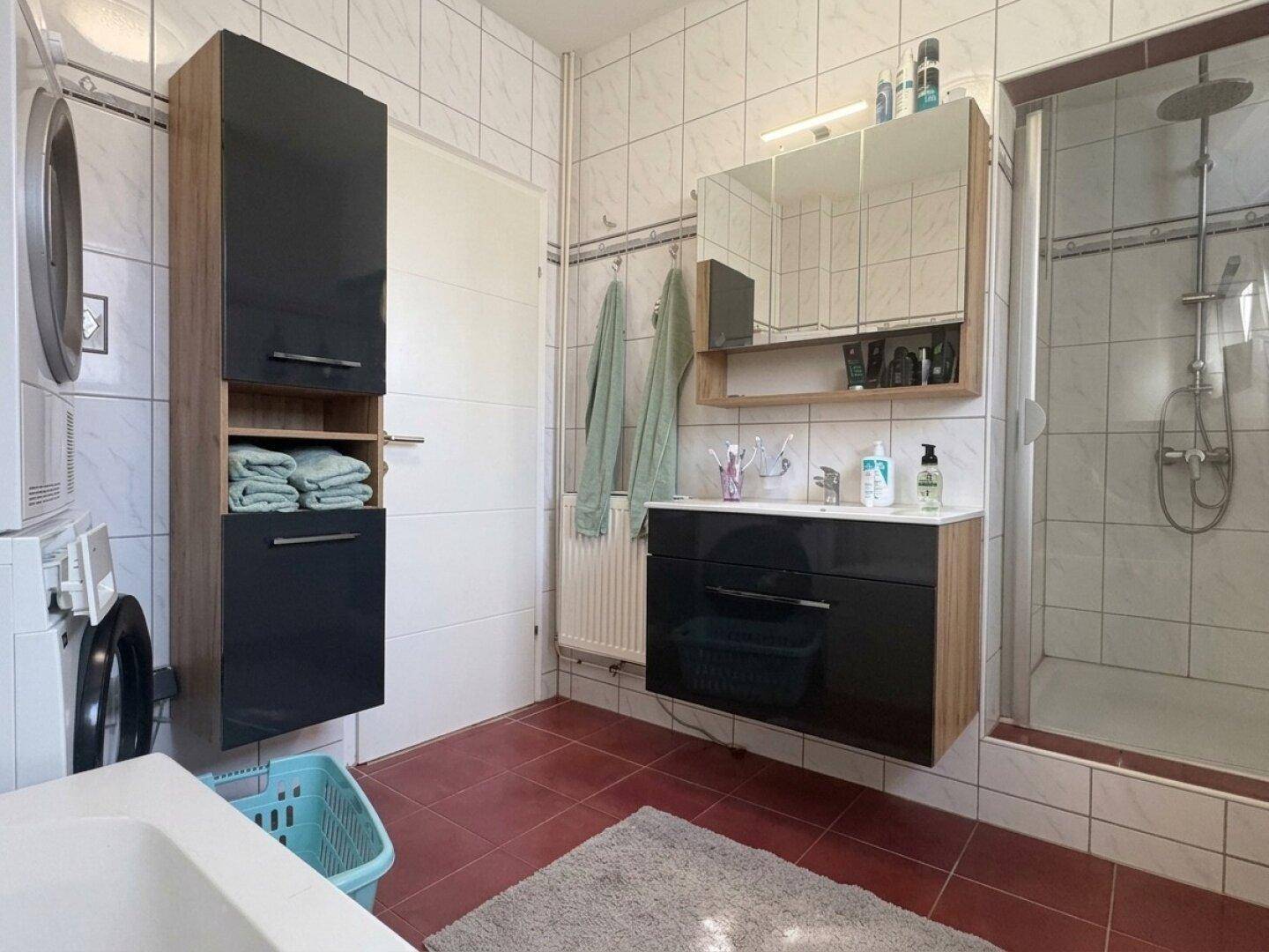 Badezimmer mit Dusche, Waschbecken, Spiegelschrank und Waschmaschine.