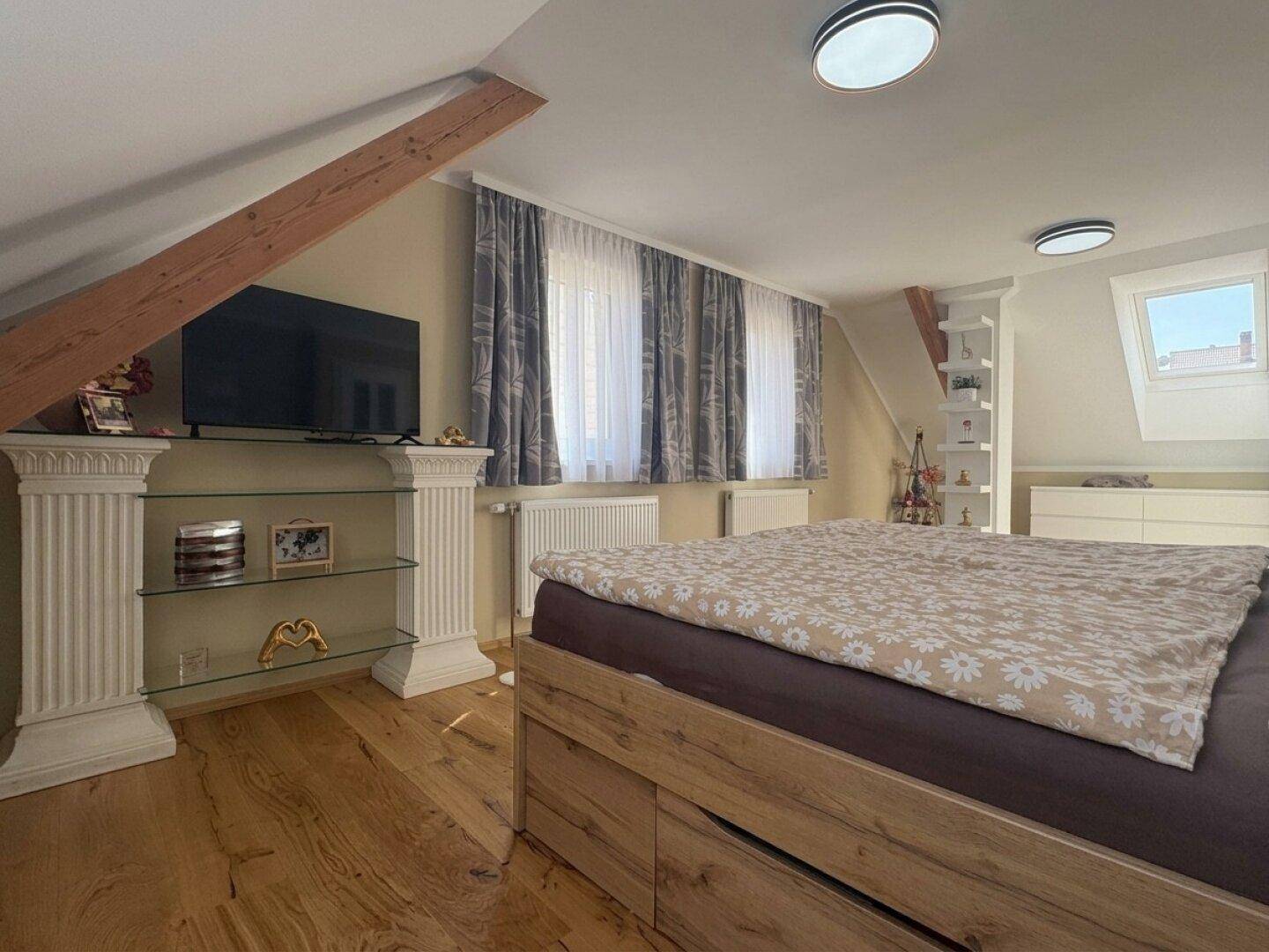 Helles Schlafzimmer im Dachgeschoss mit Holzboden, Dachfenster und modernem Bett mit Stauraum.