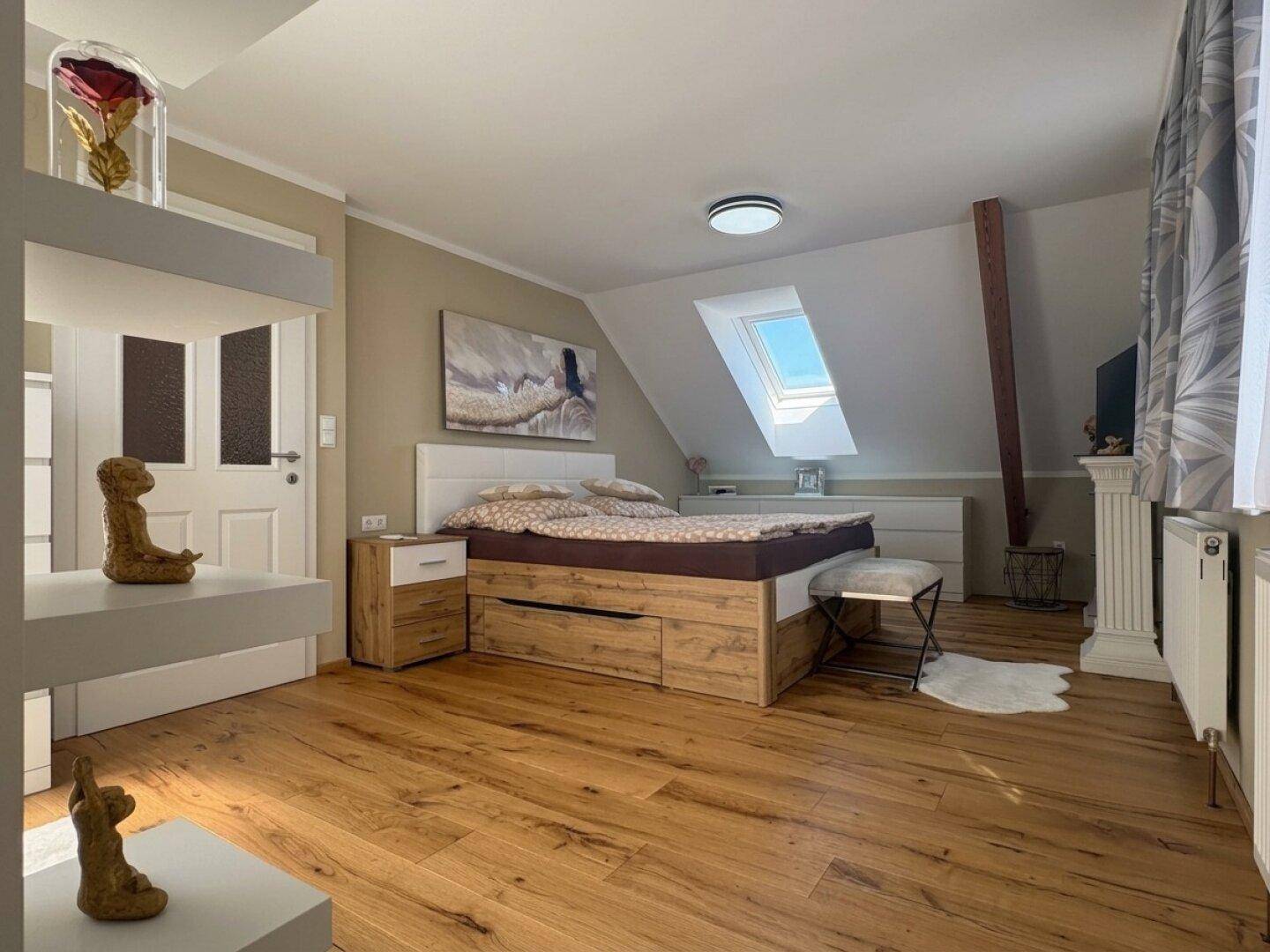 Helles Schlafzimmer im Dachgeschoss mit Holzboden, Dachfenster und modernem Bett mit Stauraum.