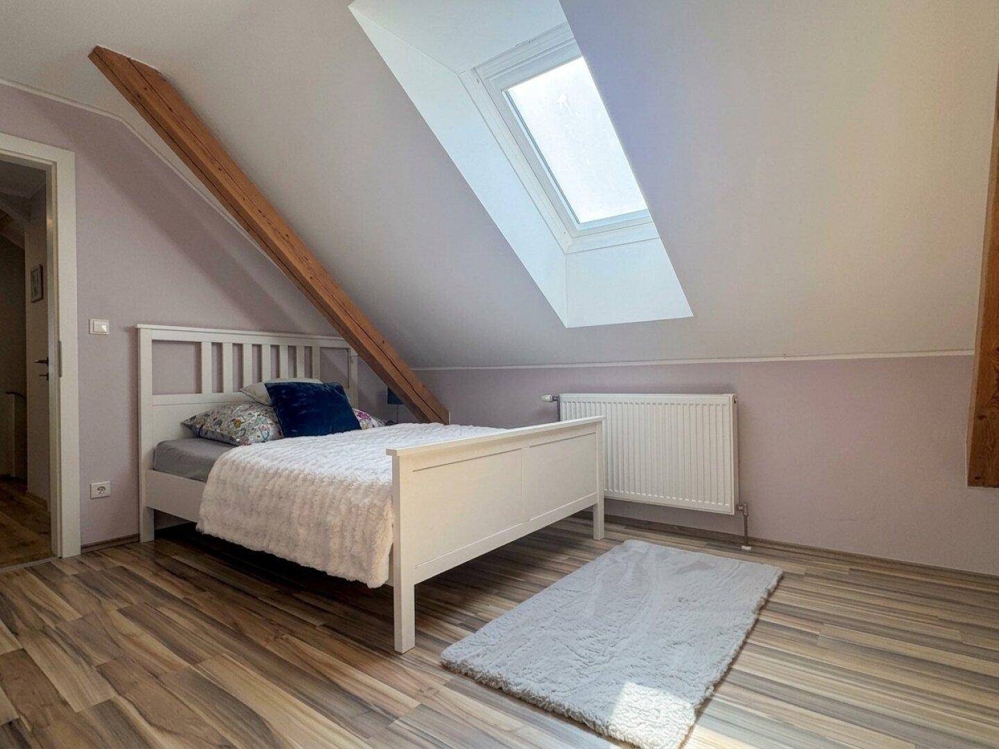 Gemütliches Schlafzimmer im Dachgeschoss mit Holzboden, Dachfenster und weißem Bett.