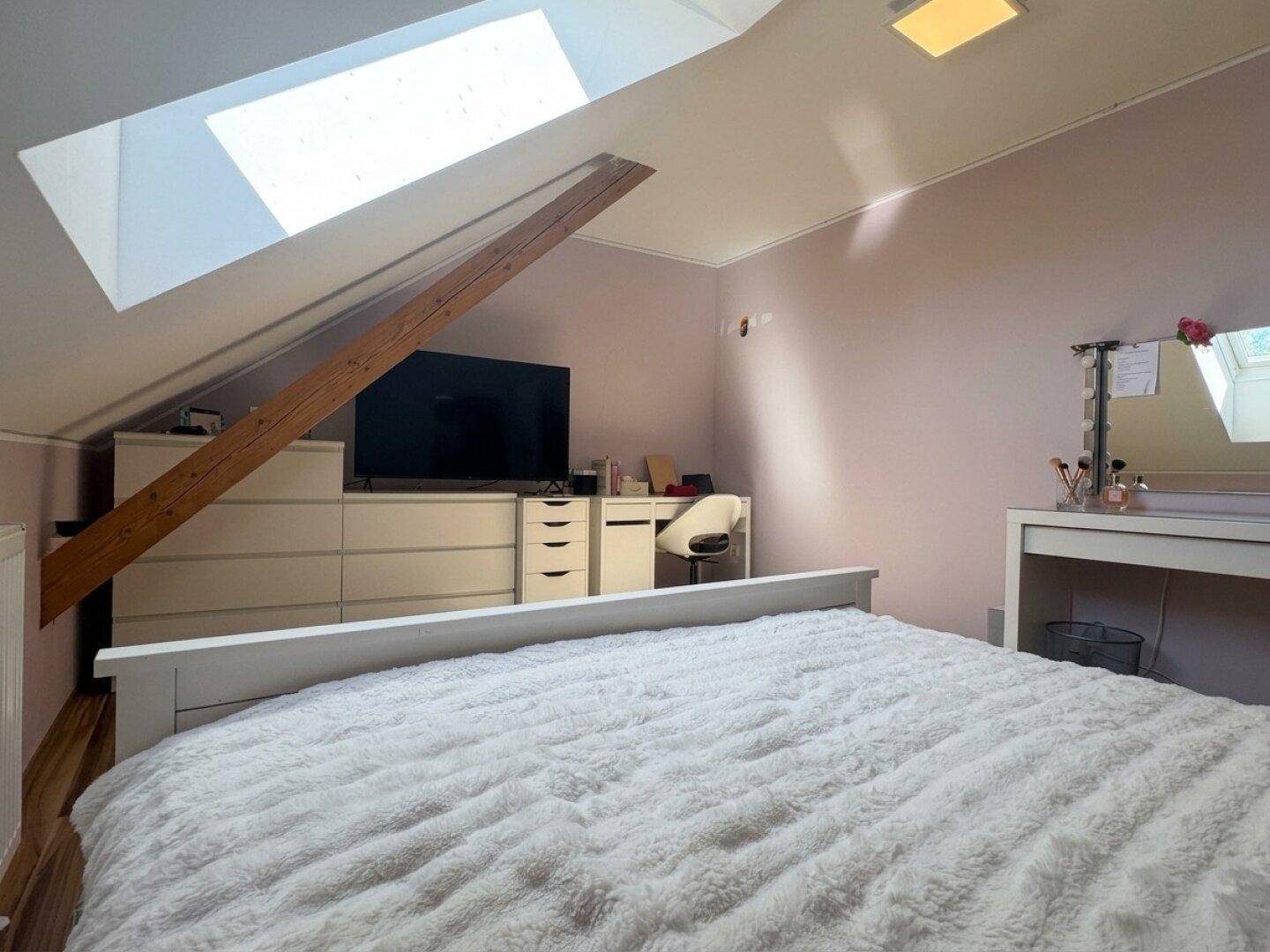 Schlafzimmer im Dachgeschoss mit Dachfenster, Schminktisch und Fernseher.
