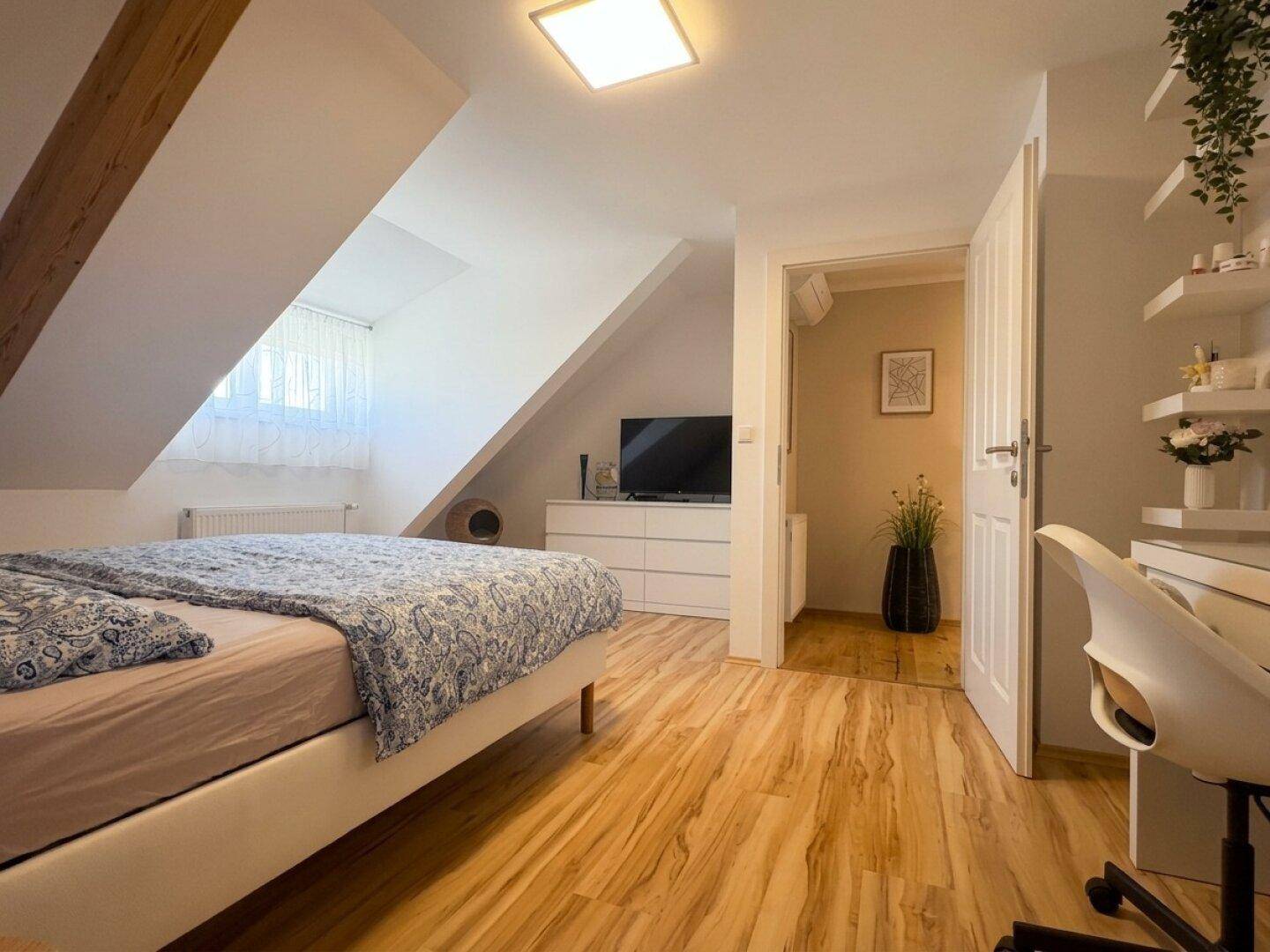 Helles Schlafzimmer im Dachgeschoss mit Holzboden, Klimaanlage und Zugang zum Flur.