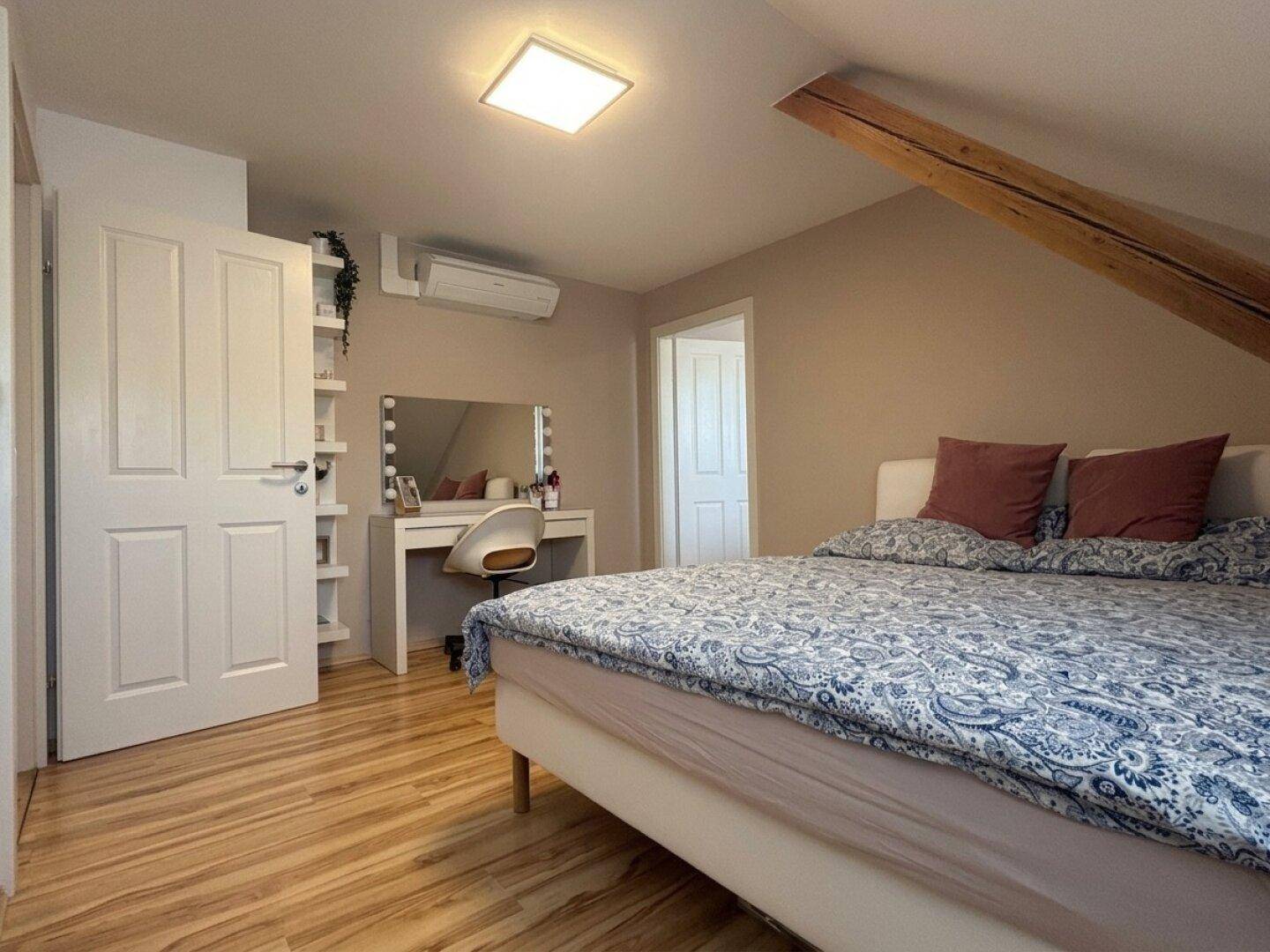 Helles Schlafzimmer im Dachgeschoss mit Holzboden, Klimaanlage und Schminktisch.