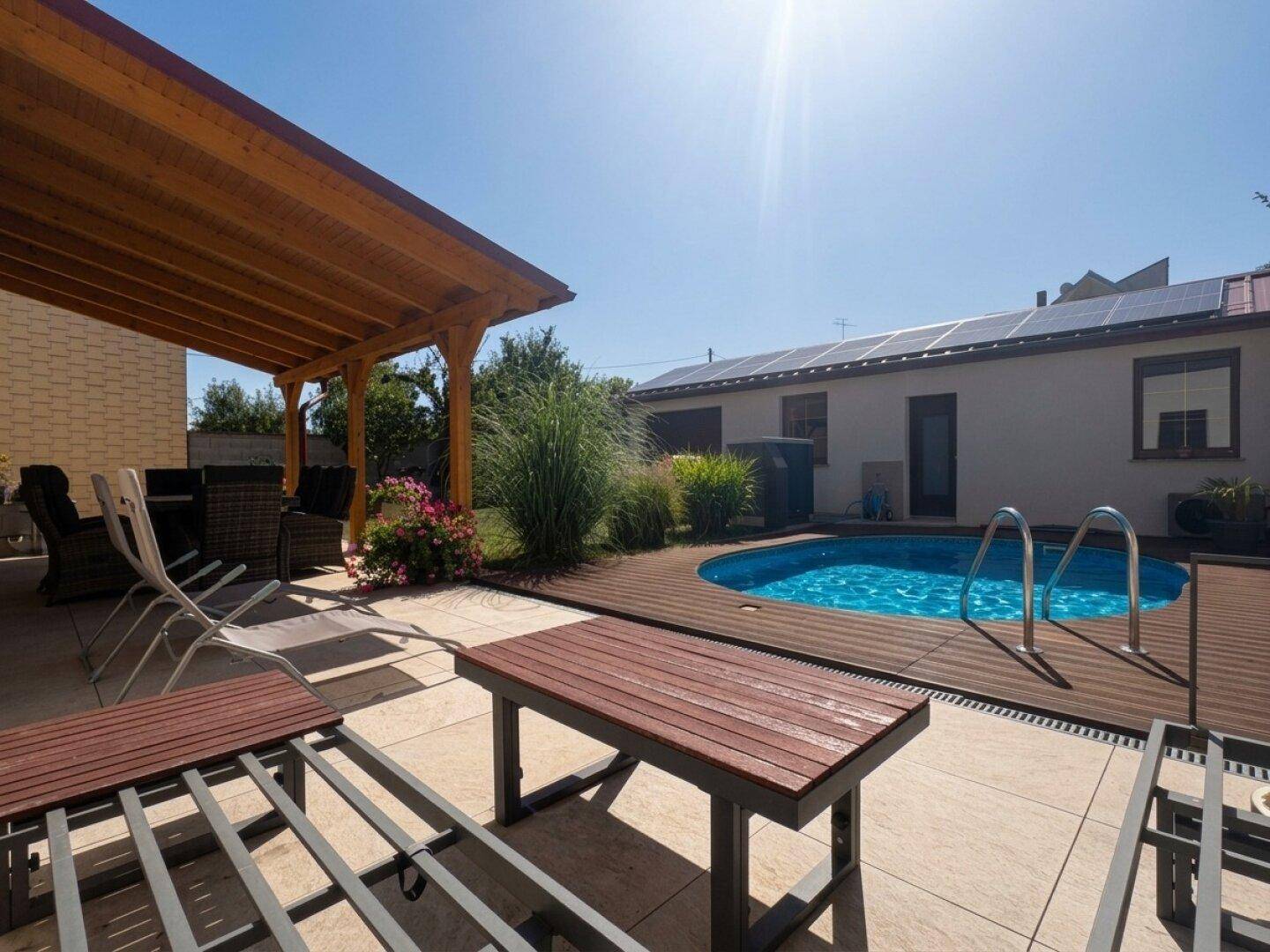 Sonniger Garten mit Pool, Holzterrasse und überdachtem Sitzbereich.