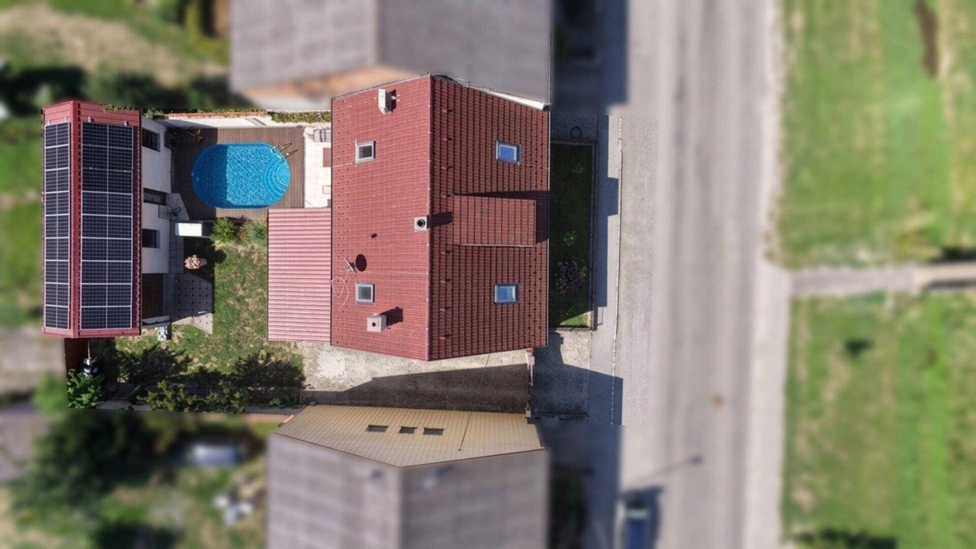 Luftaufnahme eines Hauses mit rotem Ziegeldach, Swimmingpool und Solaranlage auf dem Nebengebäude.
