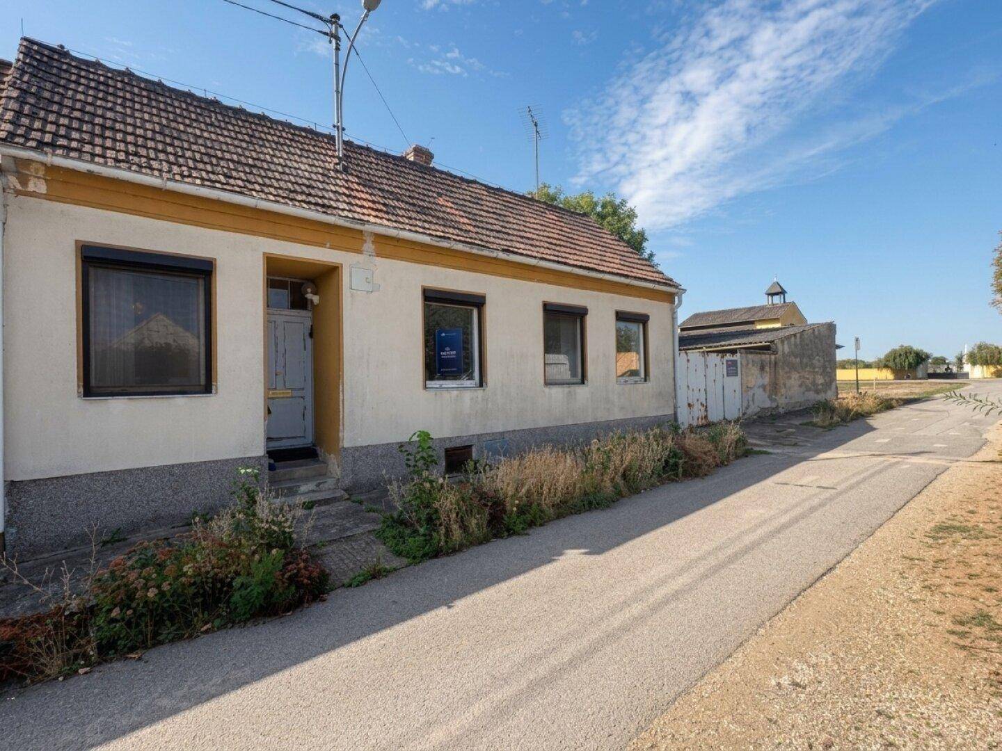 Fassade eines älteren Einfamilienhauses mit Ziegeldach und schmaler Straße davor.