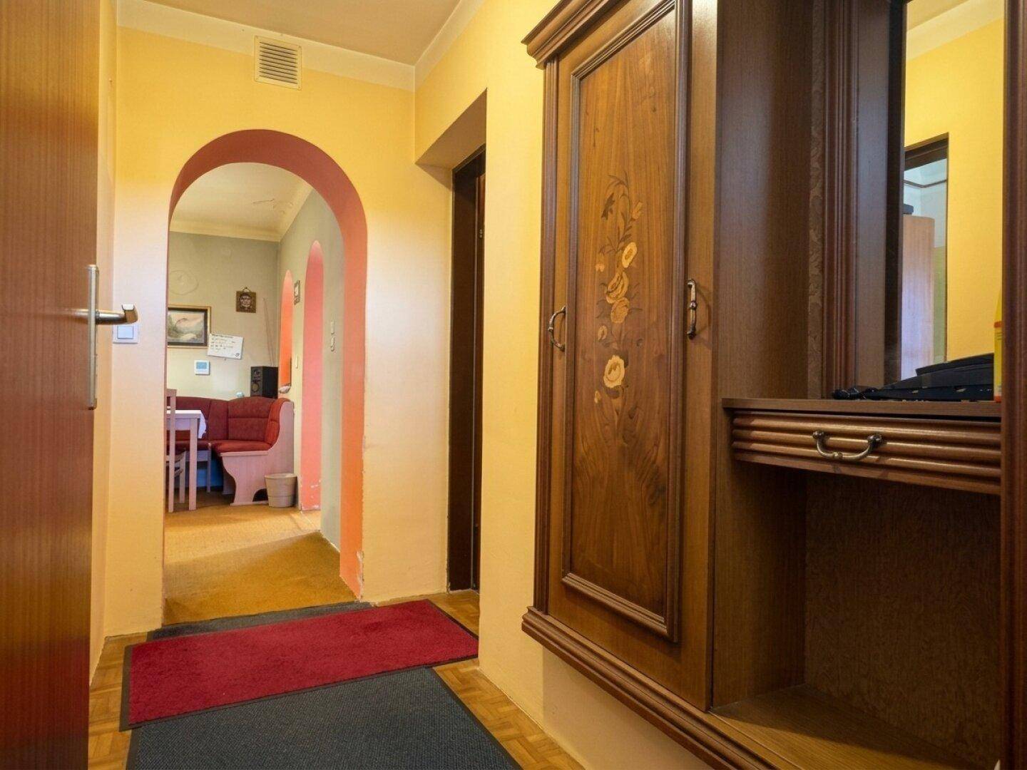 Flur mit gelben und orangefarbenen Wänden, einem Holzkabinett und einem Bogen zu einem weiteren Raum.