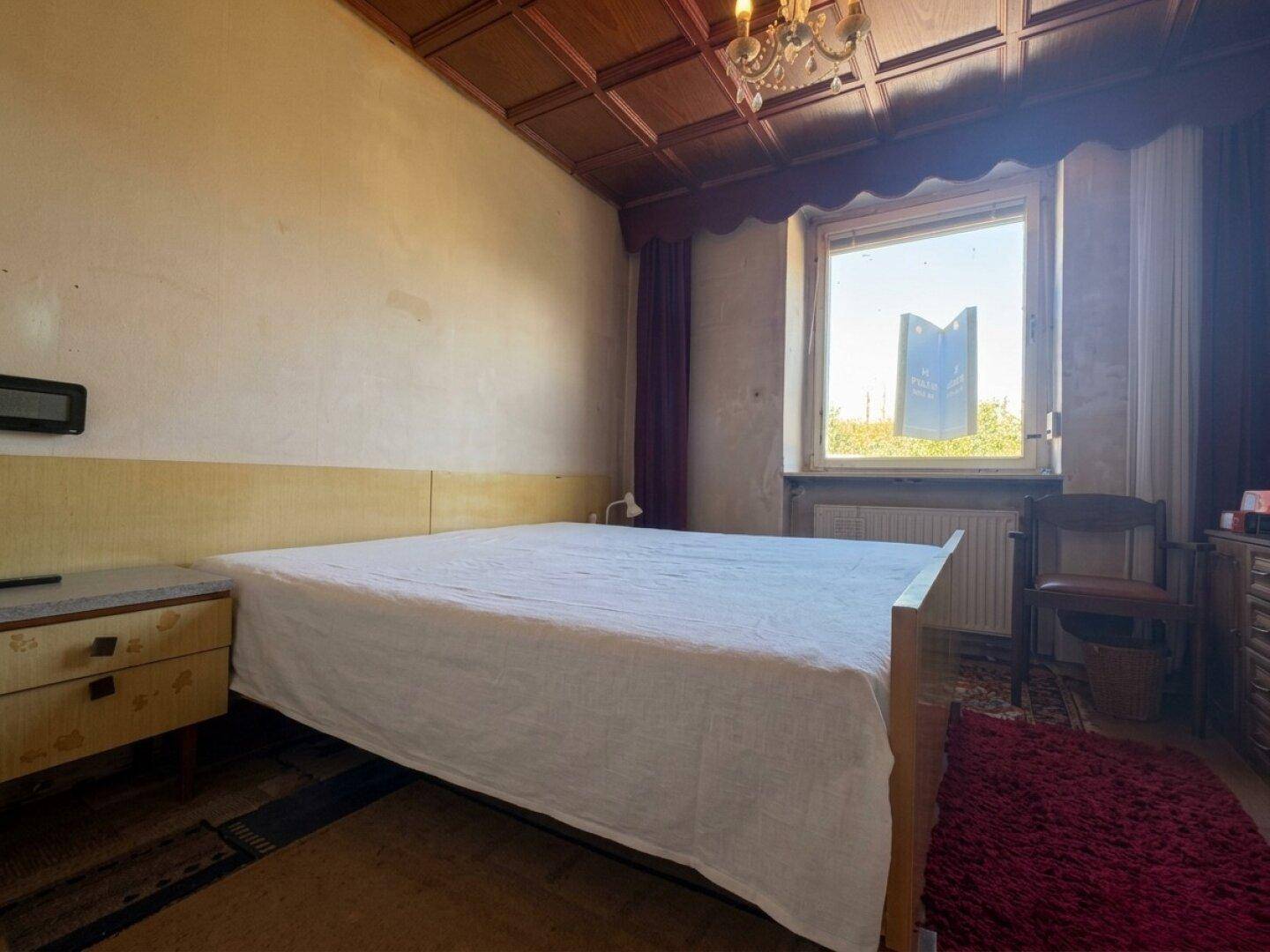 Schlafzimmer mit Doppelbett, Holzdecke und einem Fenster, das Tageslicht hereinlässt.