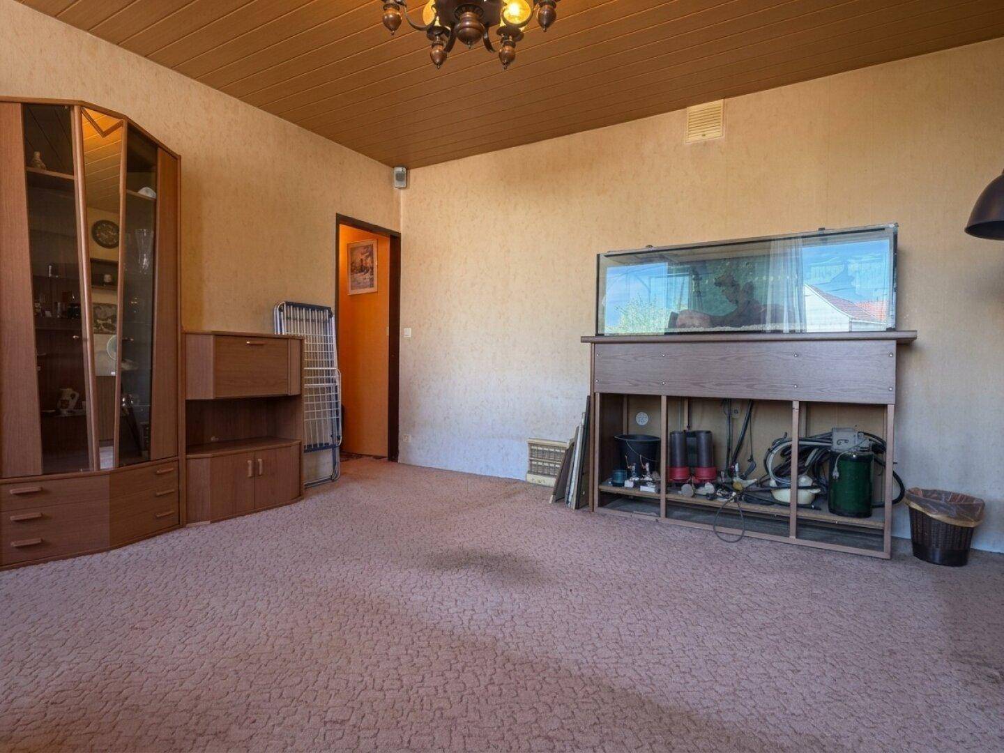 Geräumiges Wohnzimmer mit Teppichboden, Holzmöbeln und einem großen Aquarium als Blickfang.