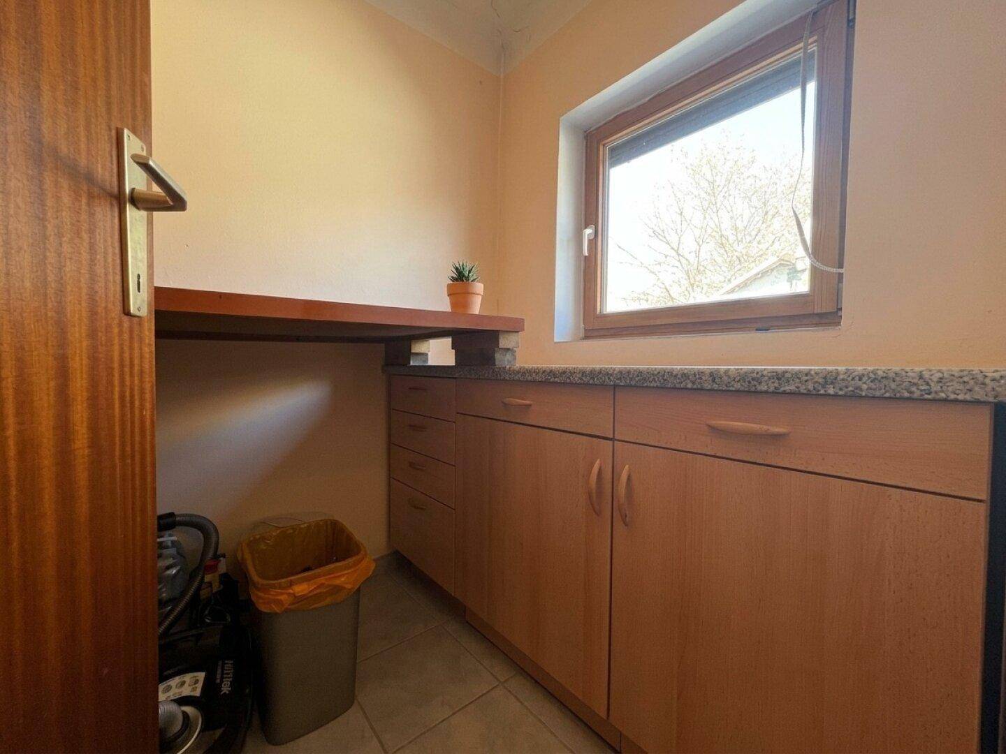 Küchenbereich mit Holzschränken, Arbeitsfläche und einem Fenster, das viel Tageslicht spendet.
