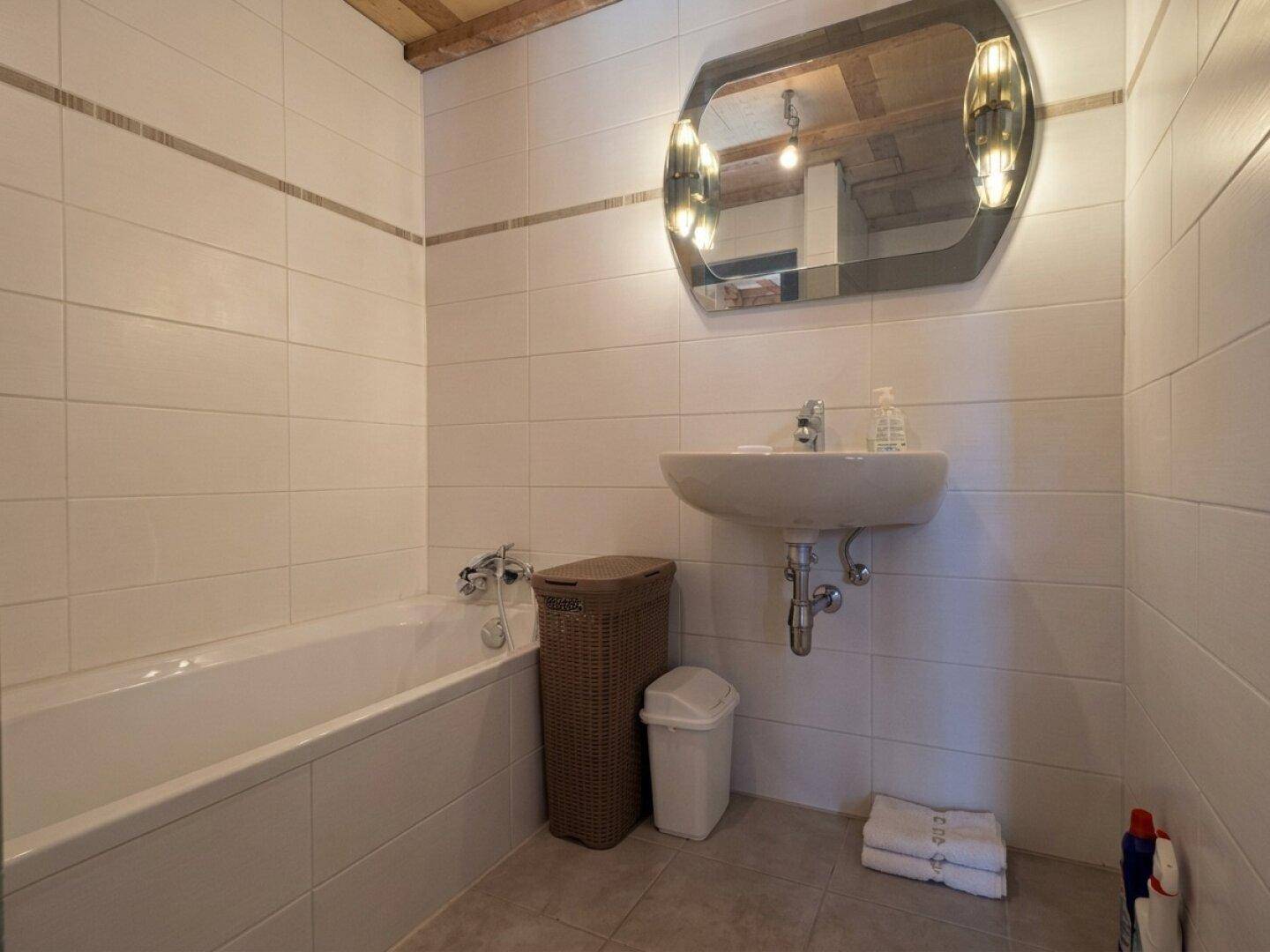 Badezimmer mit weißen Fliesen, Badewanne, Waschbecken und einem beleuchteten Spiegel.