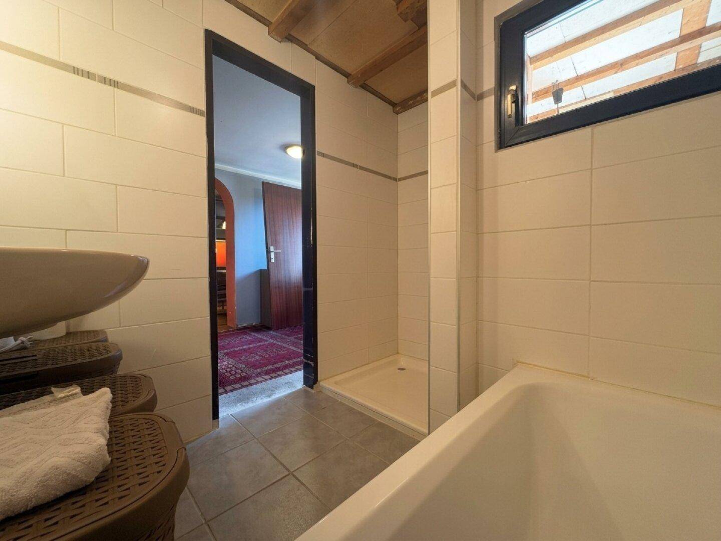 Badezimmer mit Duschbereich, Badewanne und einem Fenster, das für Belüftung sorgt.