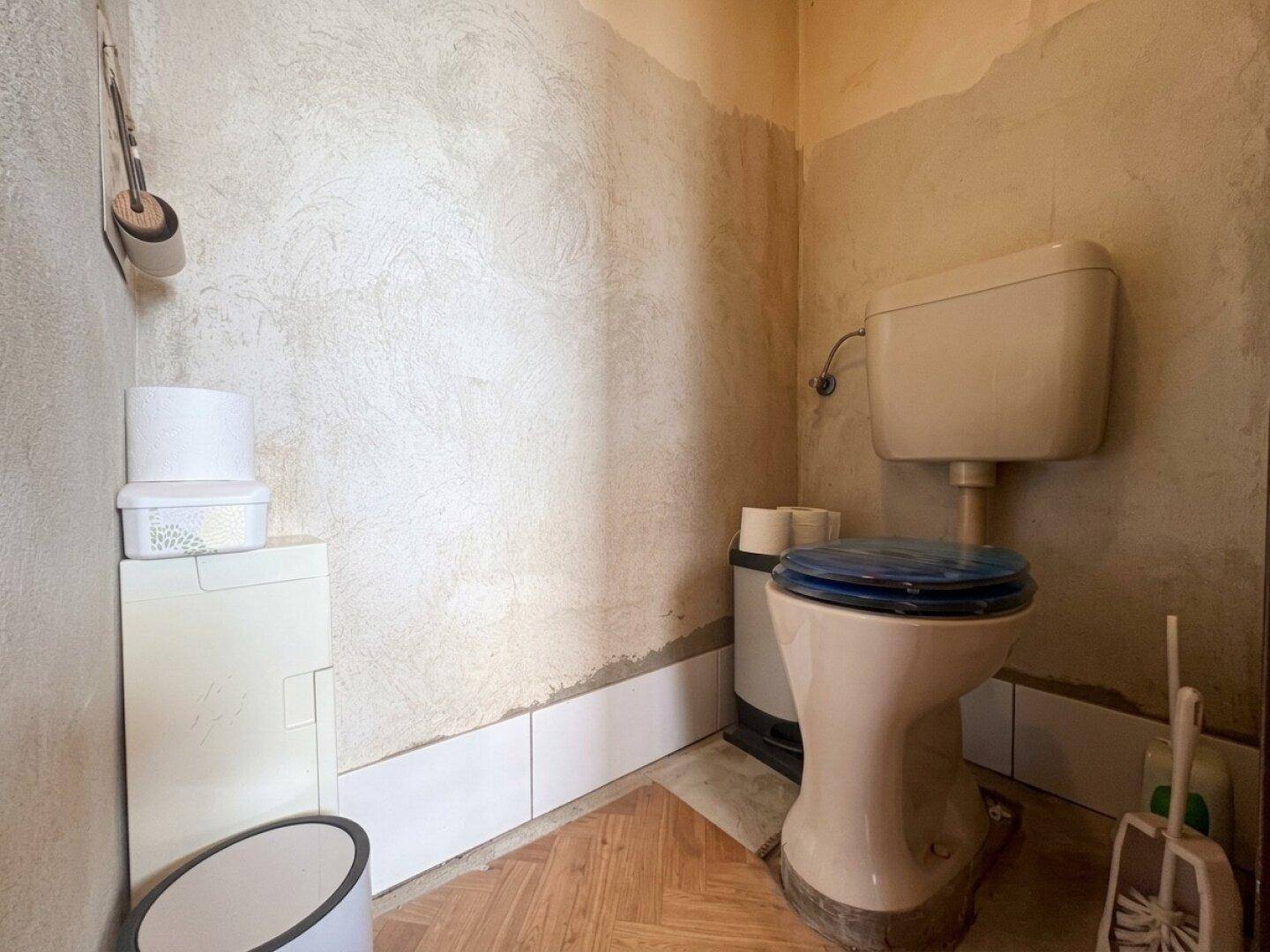 Kleiner Toilettenraum mit älterem WC und teilweise gefliesten Wänden.