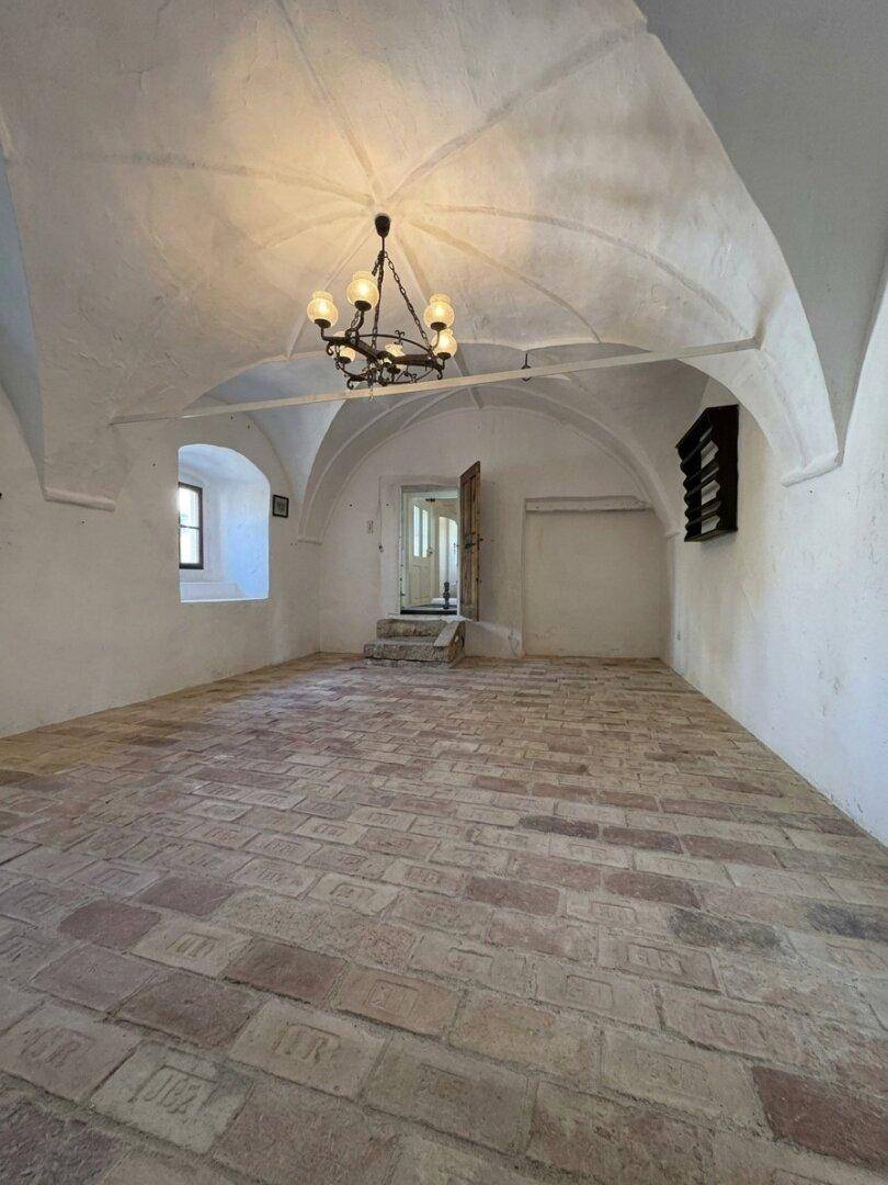 Heller Innenraum mit Gewölbedecke, Ziegelboden und einem kleinen Wandregal in einem historischen Ambiente.