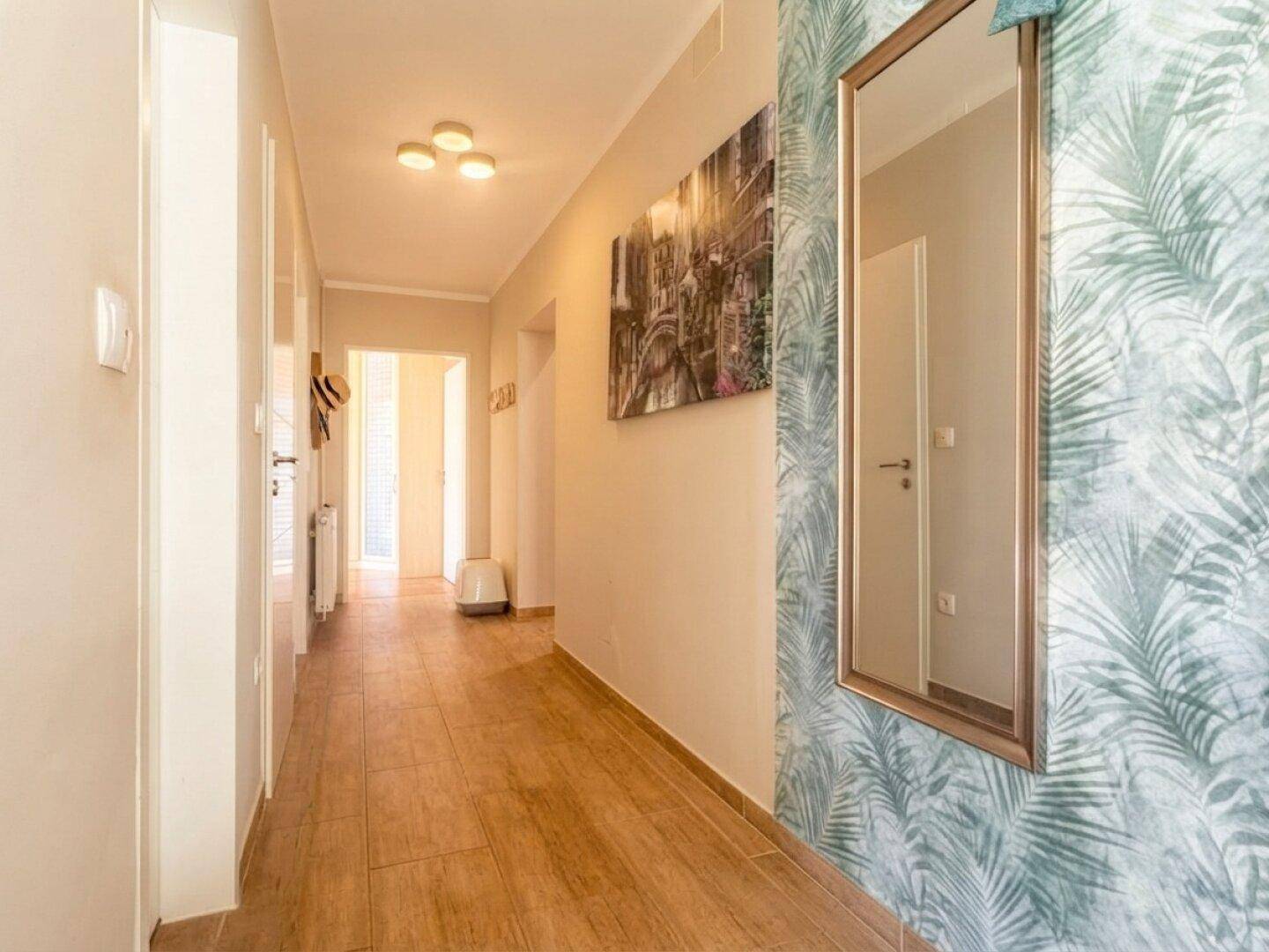 Langer Flur mit Holzoptik-Fliesen, dekorativer Tapete und großem Spiegel.