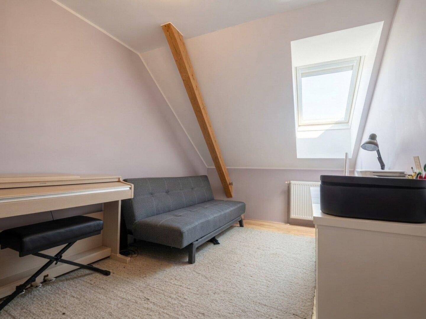 Dachgeschosszimmer mit Schlafsofa, Klavier und Dachfenster, ideal als Büro oder Gästezimmer.