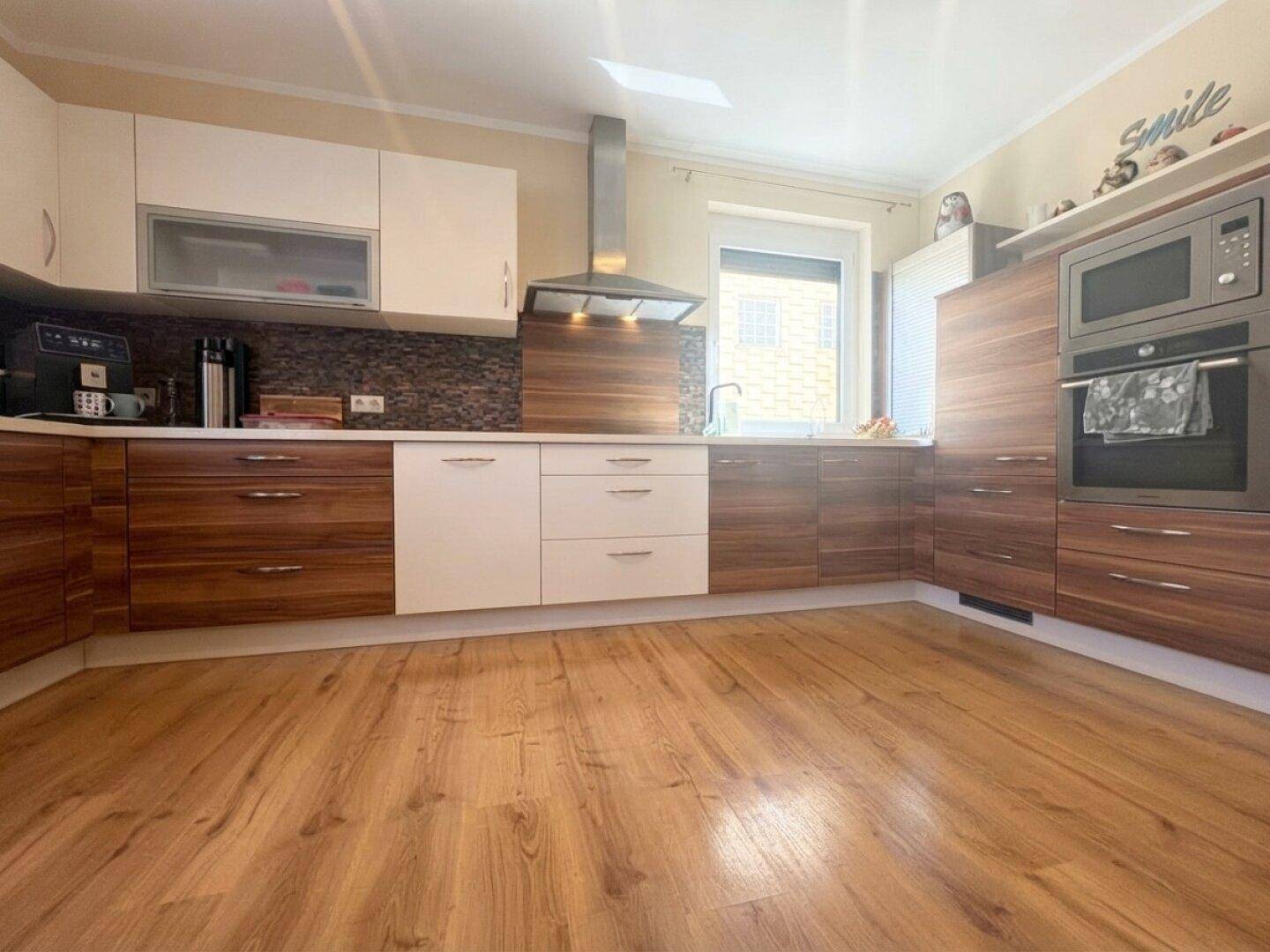 Geräumige moderne Küche mit Holz- und weißen Fronten, Einbaugeräten und Holzboden.