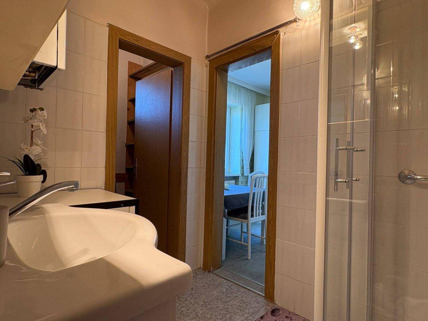 Badezimmer mit Duschkabine und Zugang zu angrenzenden Räumen, praktisch und hell.