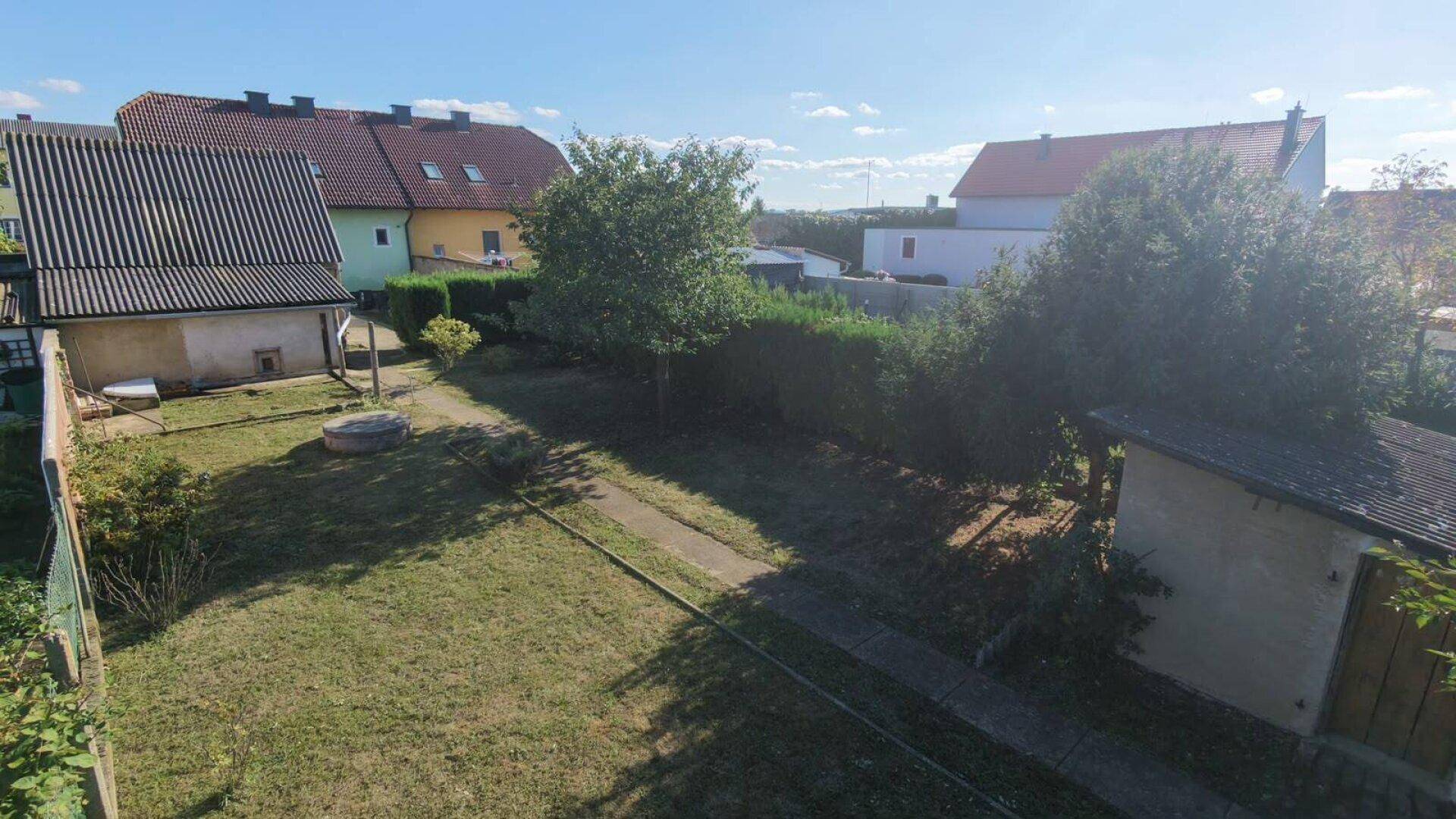 Weitläufiger Gartenbereich mit Rasenfläche, Bäumen und einem kleinen Schuppen, umgeben von Hecken.