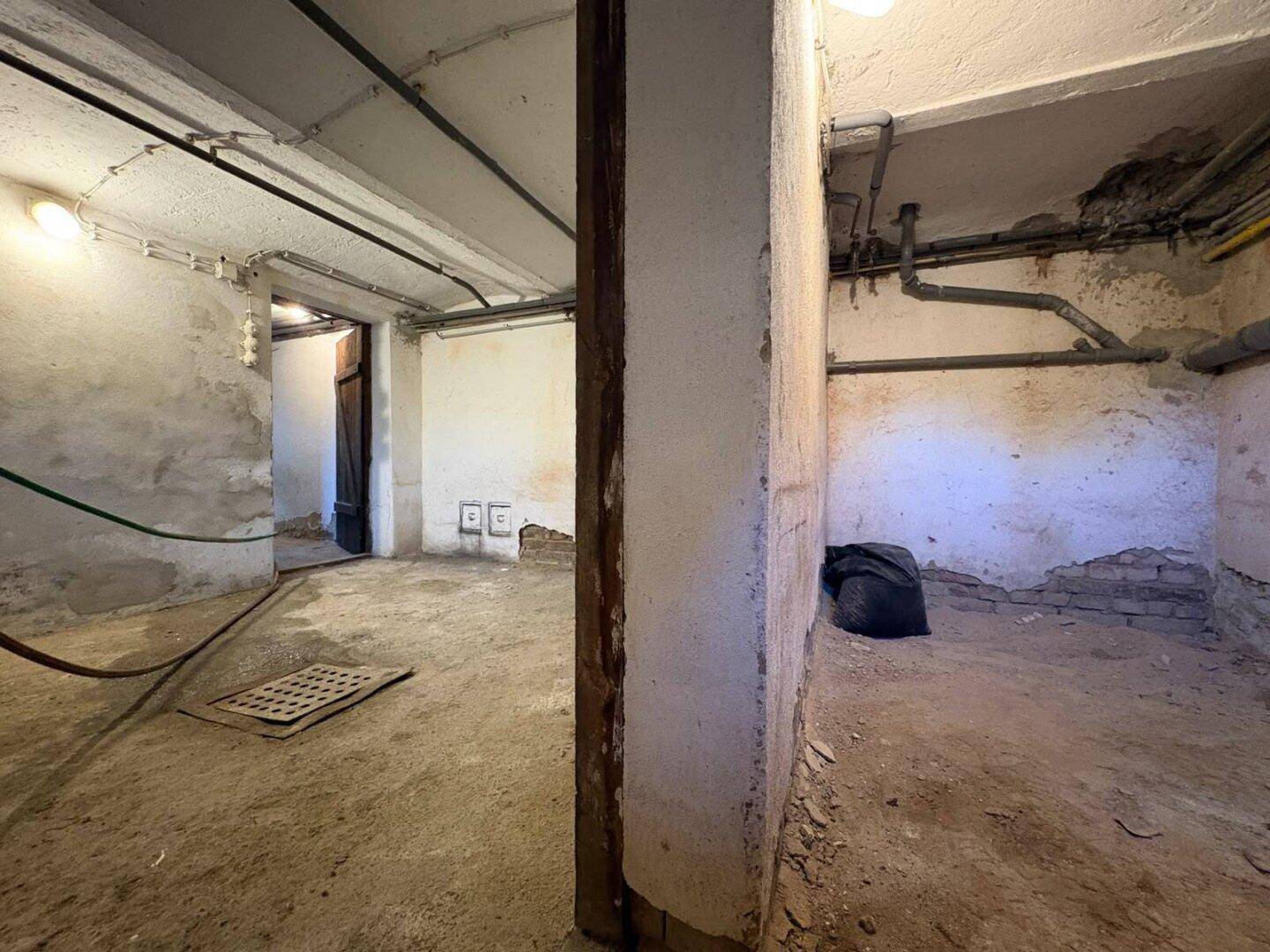 Unausgebauter Kellerraum mit sichtbaren Rohren und Betonboden, ideal als Lagerfläche.