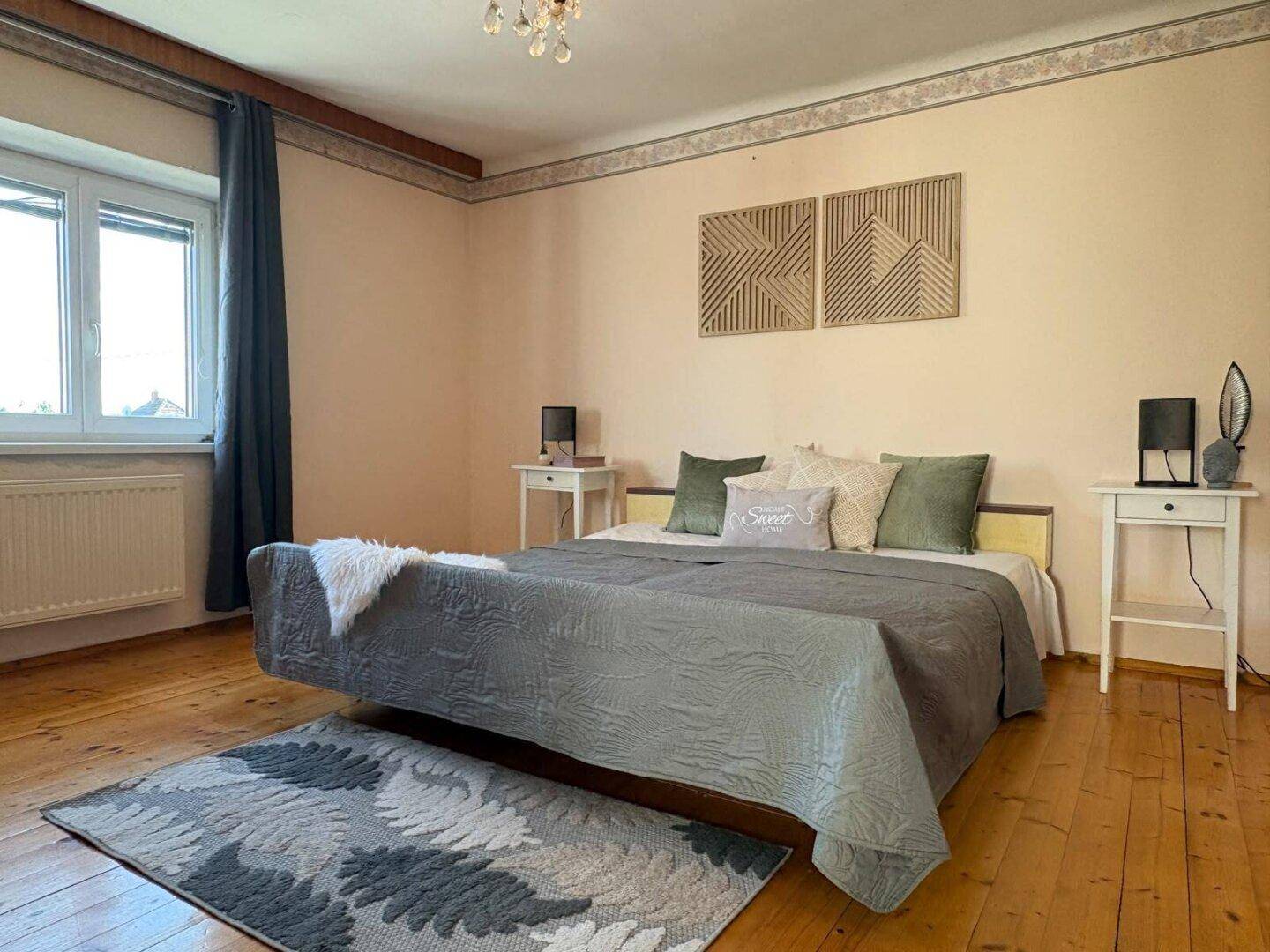 Geräumiges Schlafzimmer mit Doppelbett, Holzdielenboden und Kronleuchter, hell und einladend.
