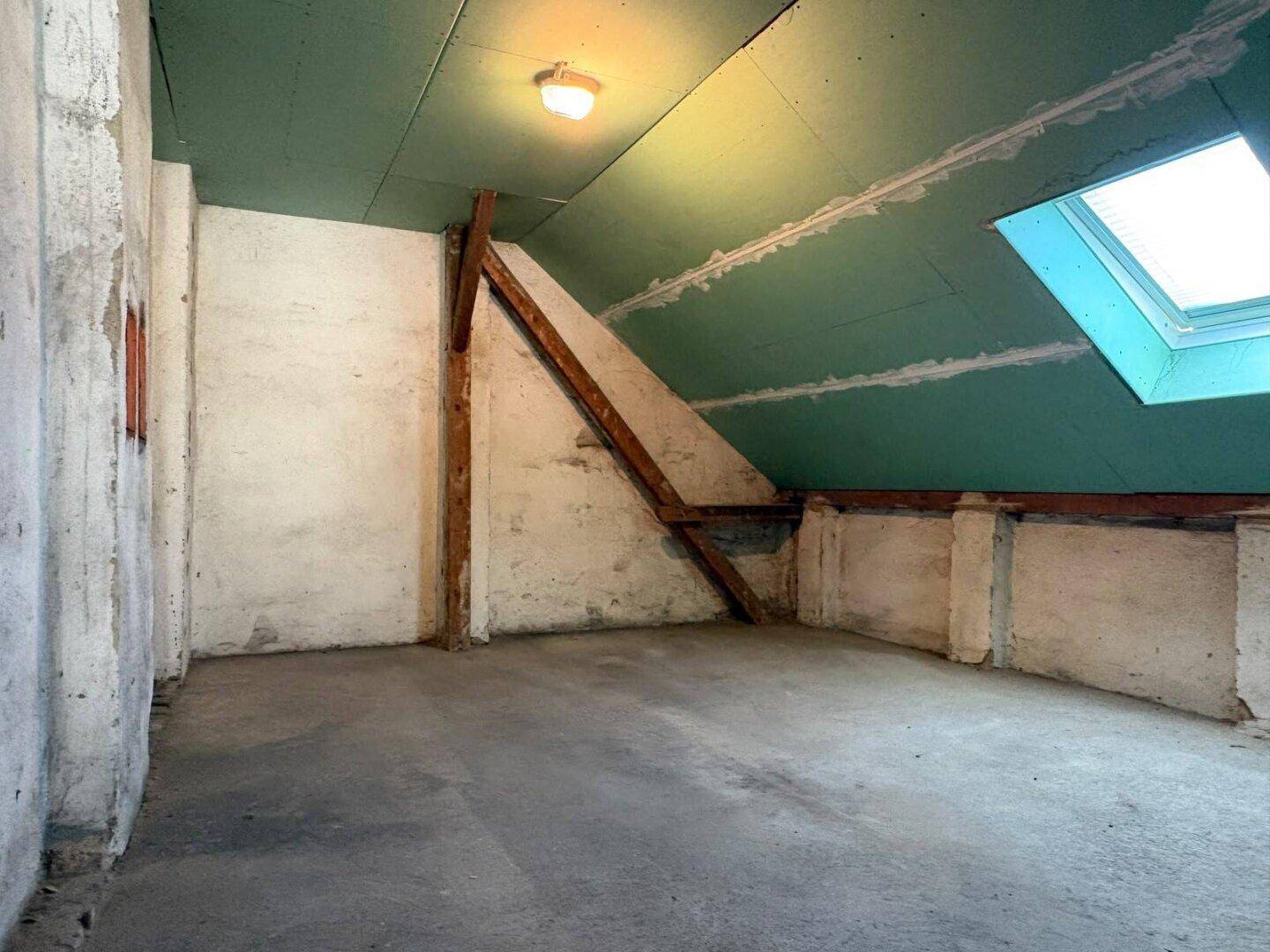 Unausgebauter Dachbodenraum mit Holzbalken und Dachfenster, bereit zum Ausbau.