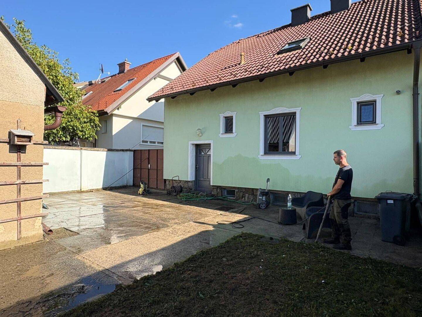 Seitenansicht des Hauses mit gepflastertem Bereich, einer Tür und einem Mann bei der Gartenarbeit.