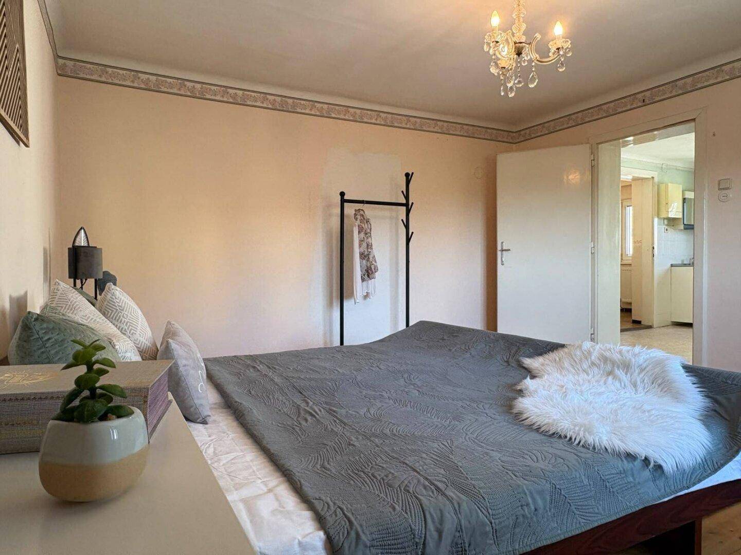 Schlafzimmer mit Doppelbett, Kronleuchter und Zugang zur Küche, gemütlich und funktional.