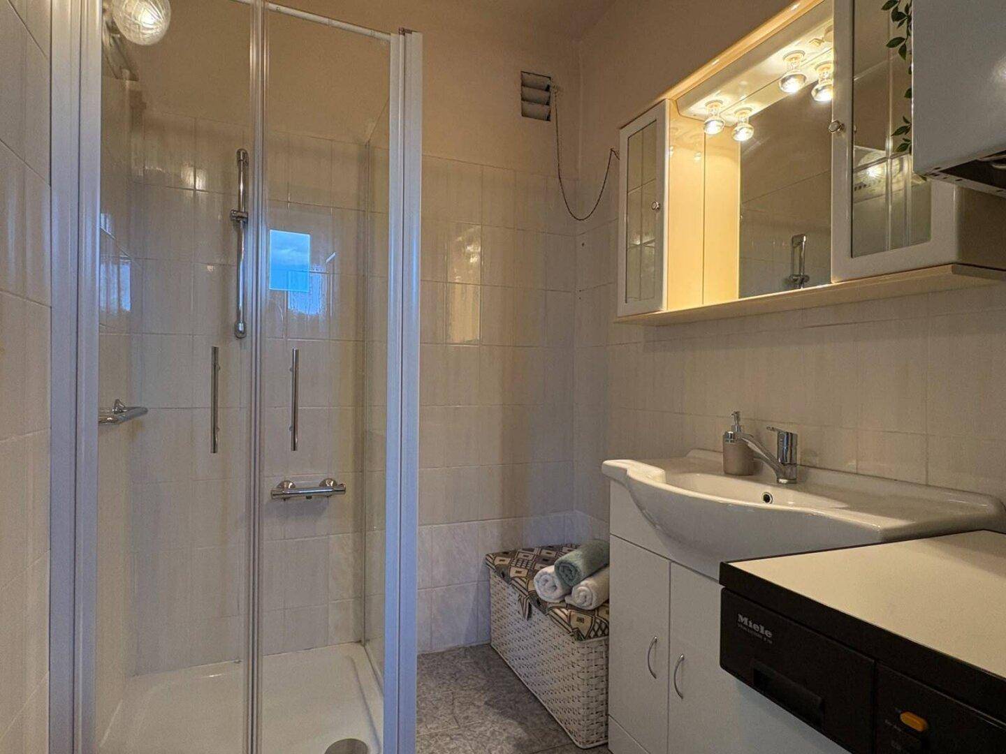 Badezimmer mit Duschkabine, Waschbecken und Spiegelschrank, hell gefliest und gepflegt.