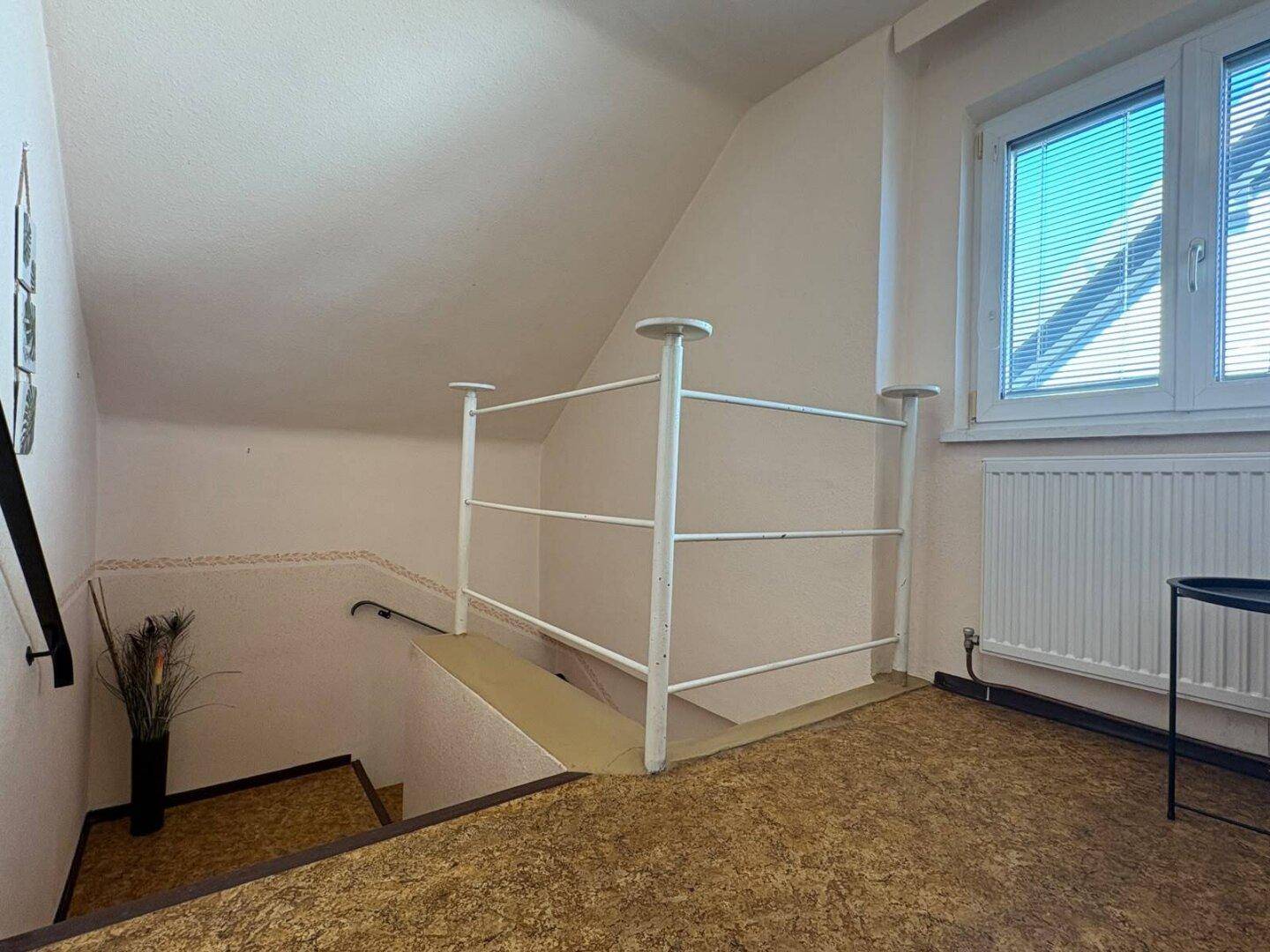 Flur mit Treppenaufgang, Fenster und Teppichboden im Dachgeschoss, hell und funktional.