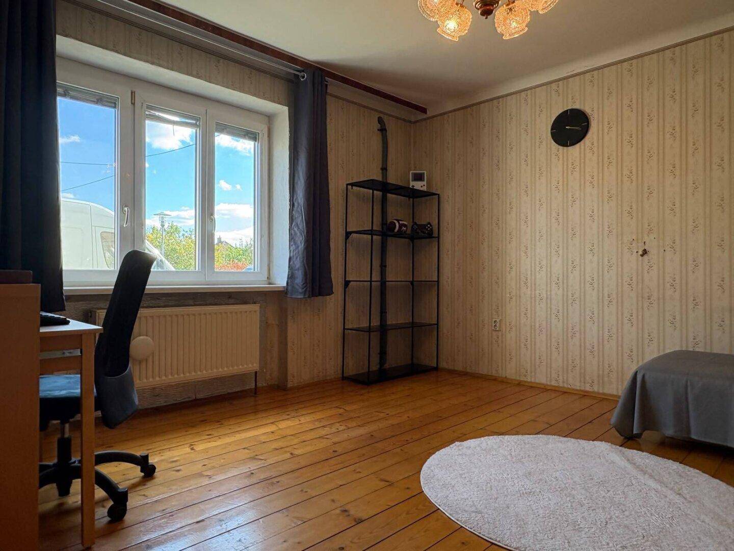 Schlafzimmer mit Holzdielenboden, Schreibtisch und gestreifter Tapete, gut beleuchtet.