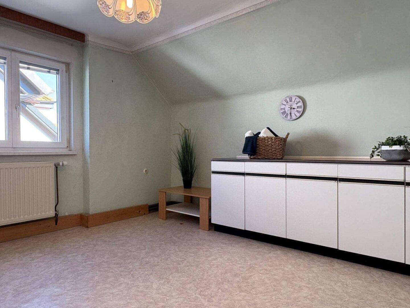 Dachgeschosszimmer mit Schräge, Fenster und Kommode, hell gestrichen und vielseitig nutzbar.